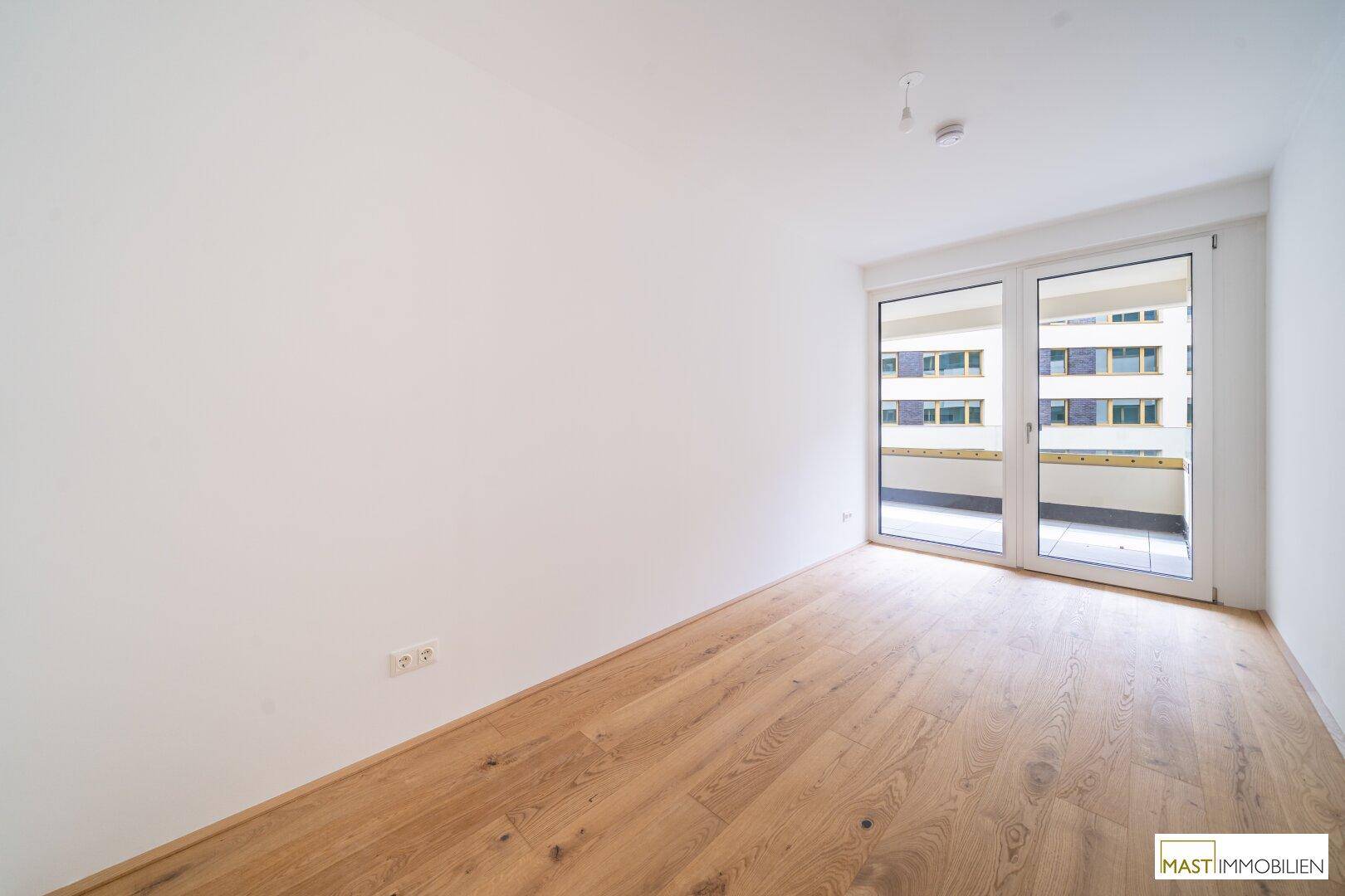 Freundliches Zimmer mit Parkettboden und großzügiger Balkontür, bietet viel Tageslicht.