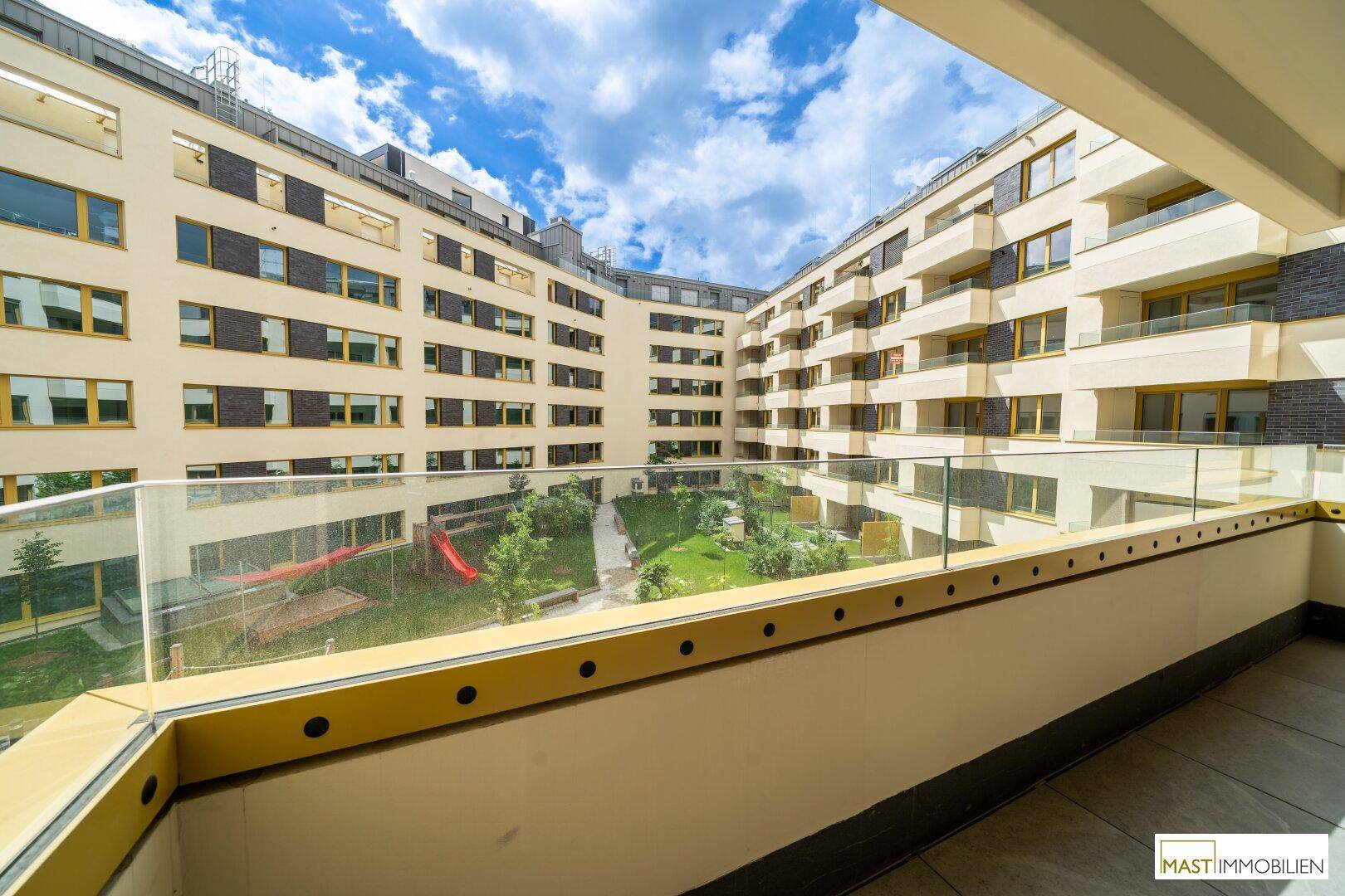 Balkon mit Blick auf den begrünten Innenhof und das moderne Wohngebäude.
