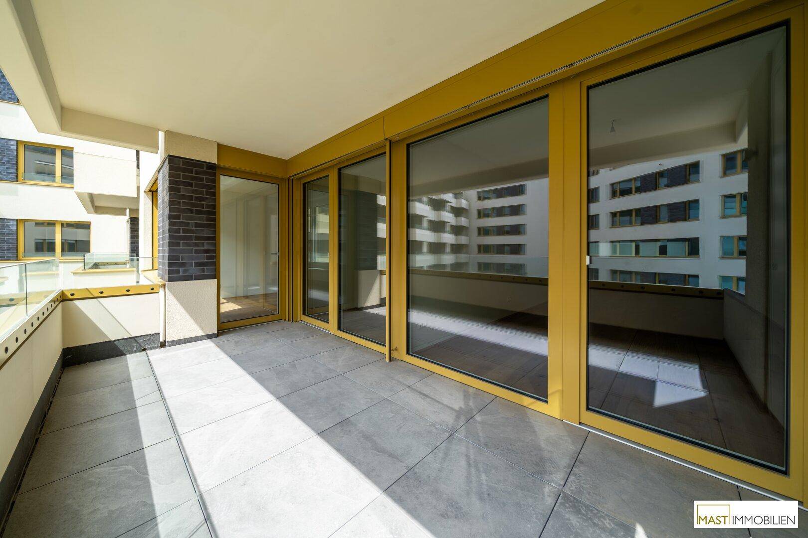Geräumiger Balkon mit Fliesenboden und Glasgeländer, ideal für entspannte Stunden im Freien.