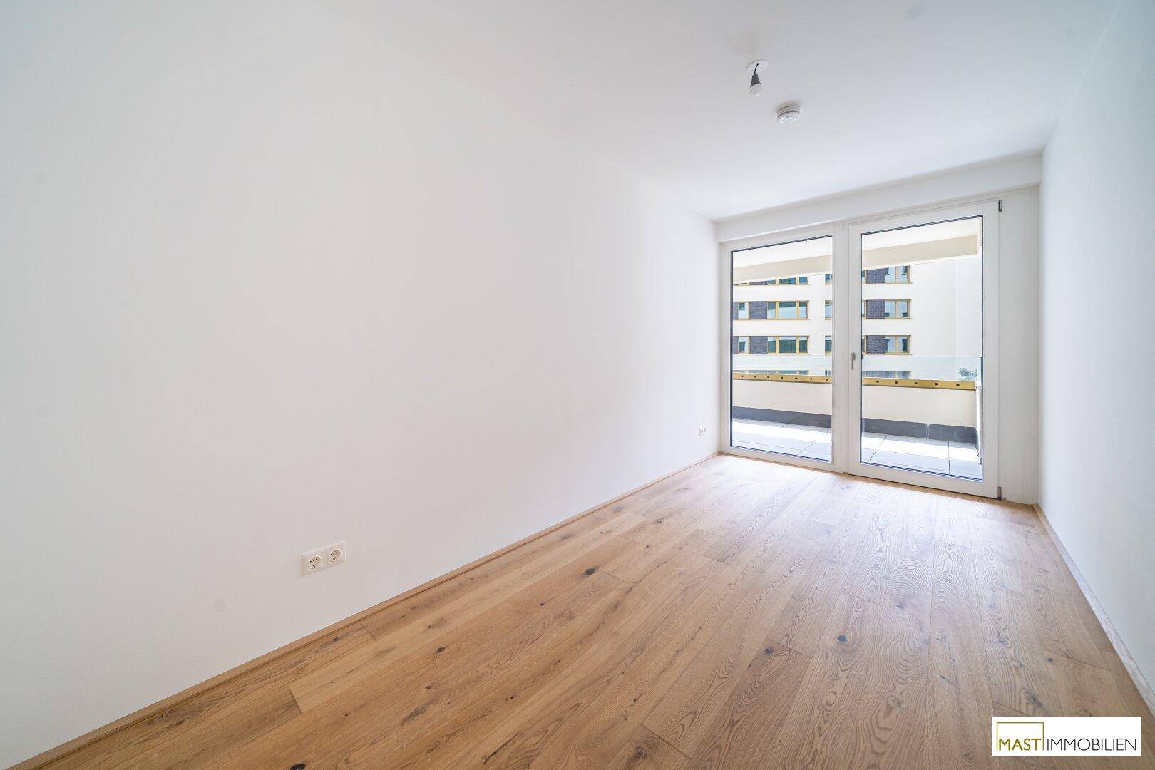 Schlafzimmer mit hellem Parkettboden und direktem Zugang zu einem Balkon, bietet viel Tageslicht.