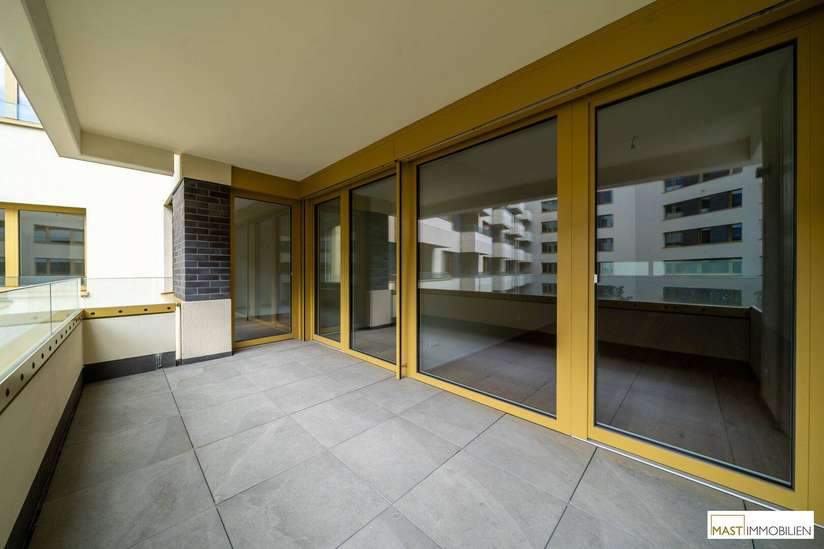 Breiter Balkon mit modernen Fliesen und großen Glasfronten, die viel Licht in die Innenräume lassen.