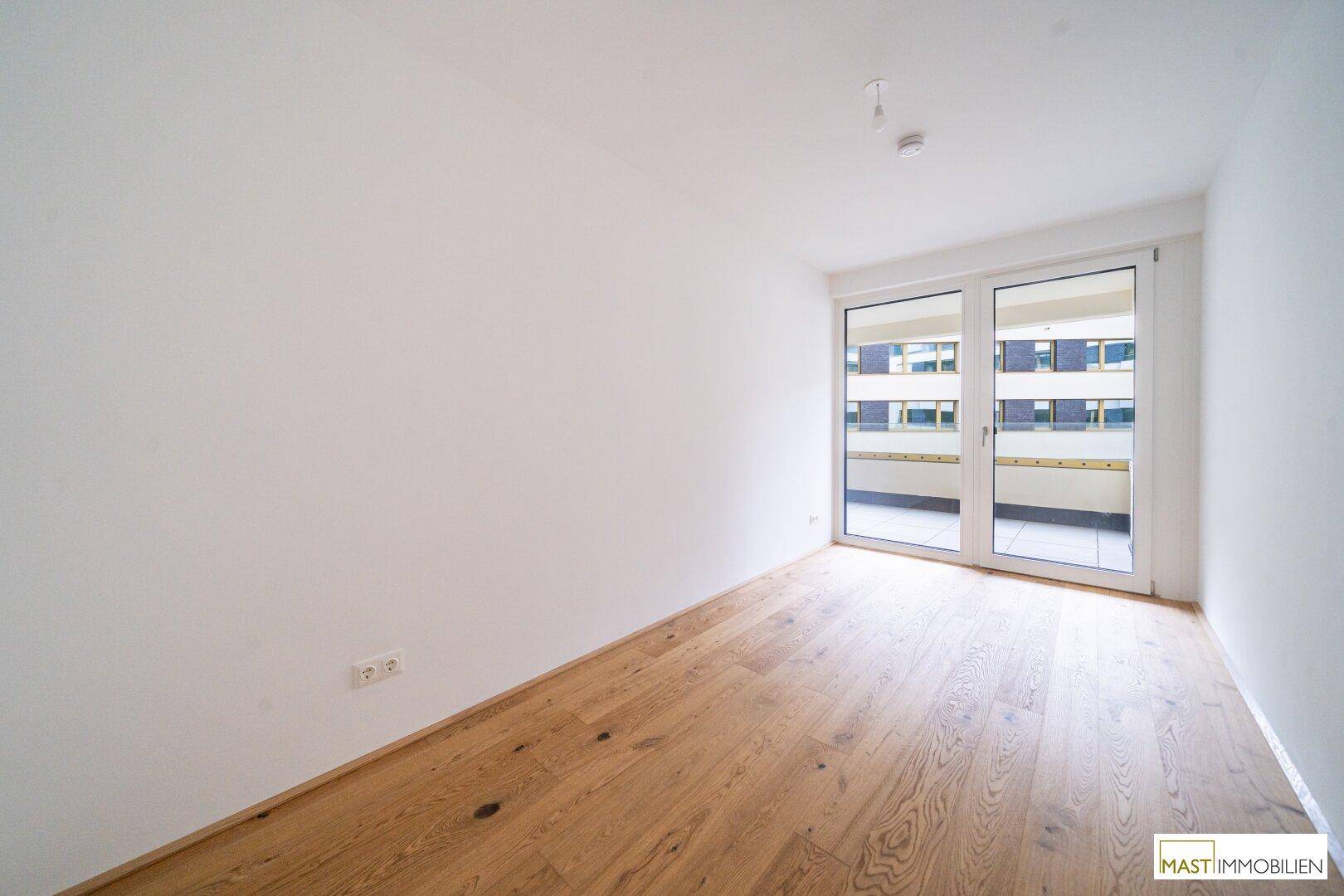 Geräumiger, heller Raum mit Holzboden und Balkonzugang, ideal für Wohn- oder Schlafbereich.