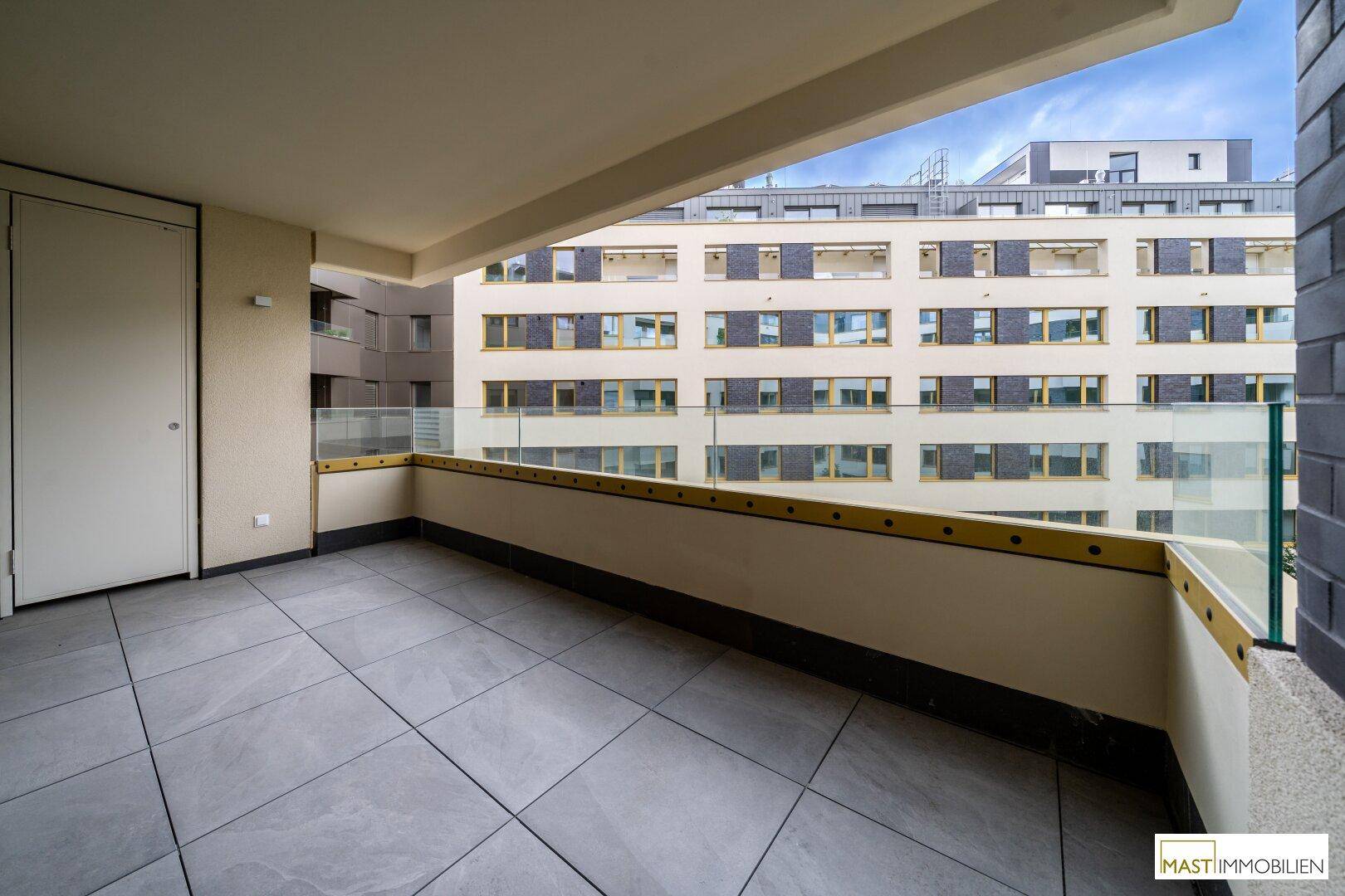 Geräumiger Balkon mit Fliesenboden und Blick auf die umliegenden Gebäude des Komplexes.