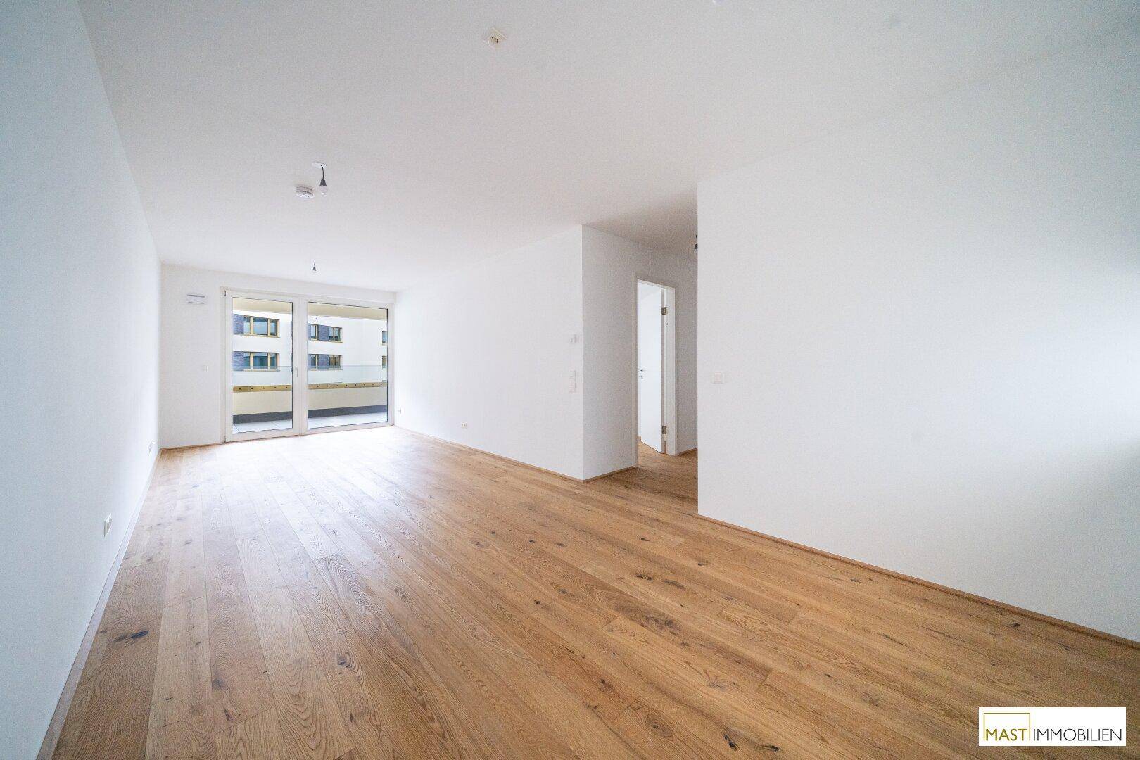 Großzügiger, heller Raum mit Holzboden und Zugang zu einem Balkon, bietet vielseitige Nutzungsmöglichkeiten.