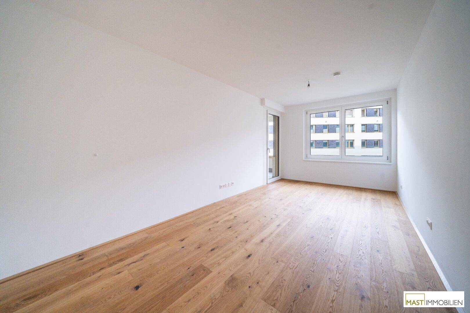 Freundliches Zimmer mit Holzboden und großem Fenster, ideal als Schlafzimmer oder Arbeitsbereich.