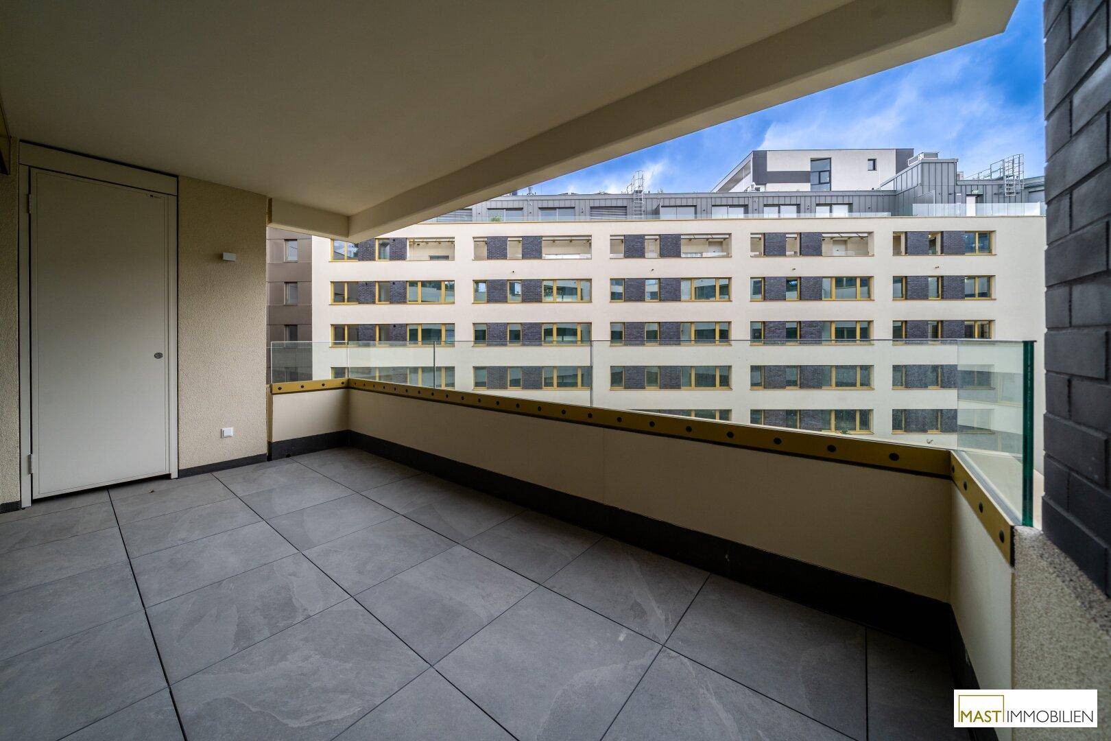 Heller Balkon mit Glasgeländer und Fliesenboden, bietet einen weiten Blick auf die Nachbarschaft.