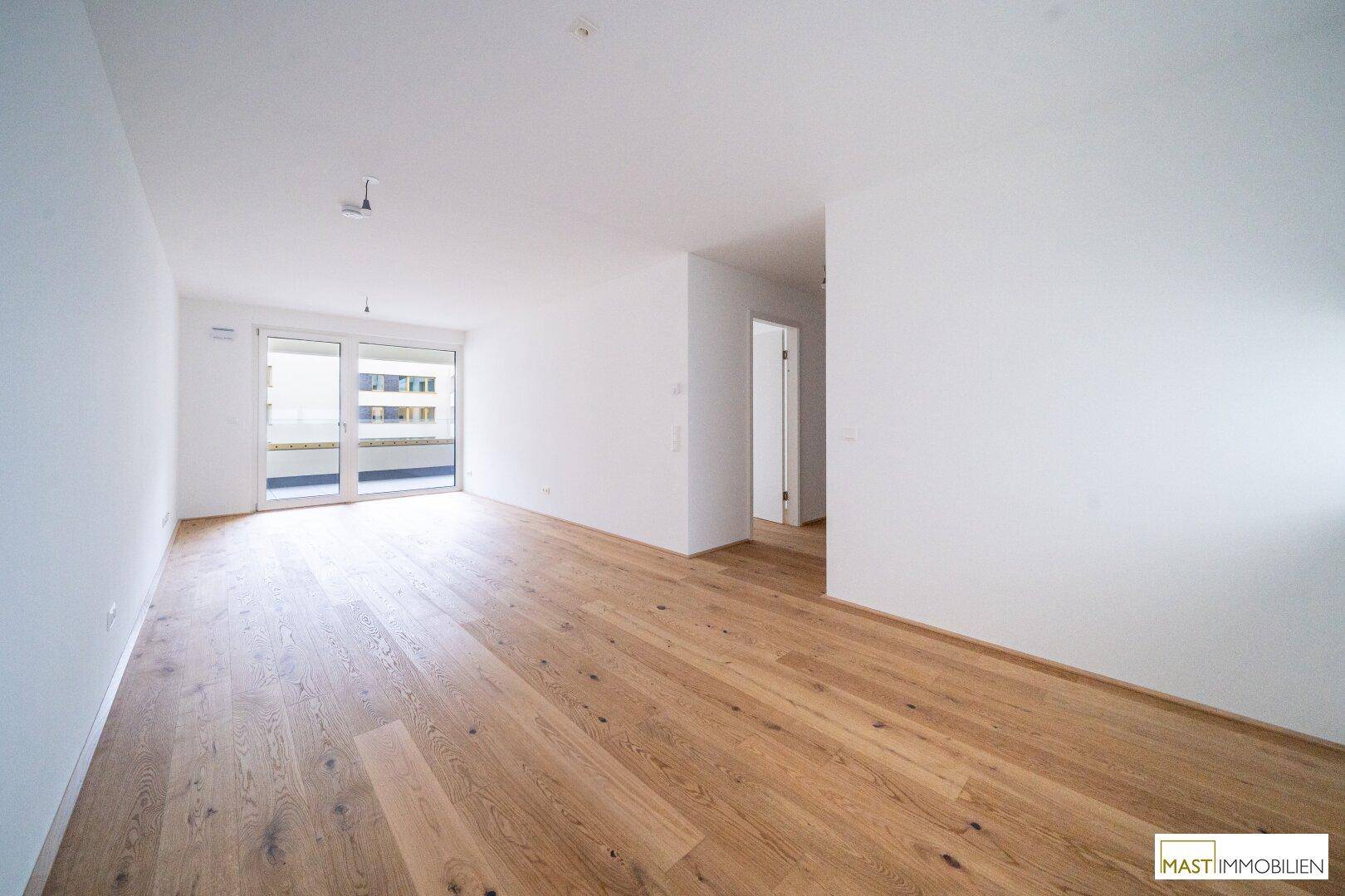 Lichtdurchfluteter Raum mit Holzboden und Zugang zum Balkon, ideal für einen Wohnbereich.