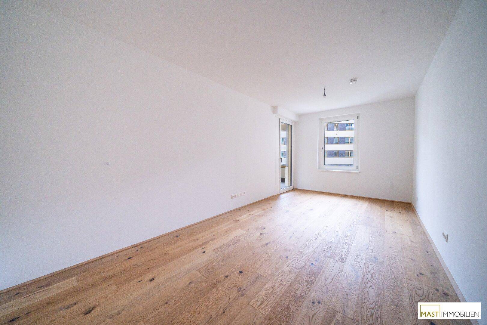 Helles Schlafzimmer mit Parkettboden und Fenster, das viel Tageslicht in den Raum lässt.