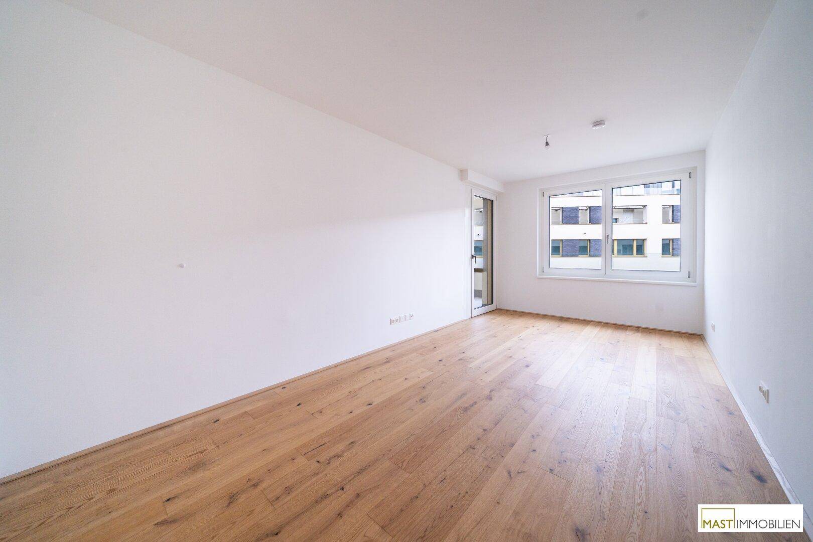 Helles, leeres Zimmer mit Eichenparkettboden und einem großen Fenster, das viel Tageslicht hereinlässt.