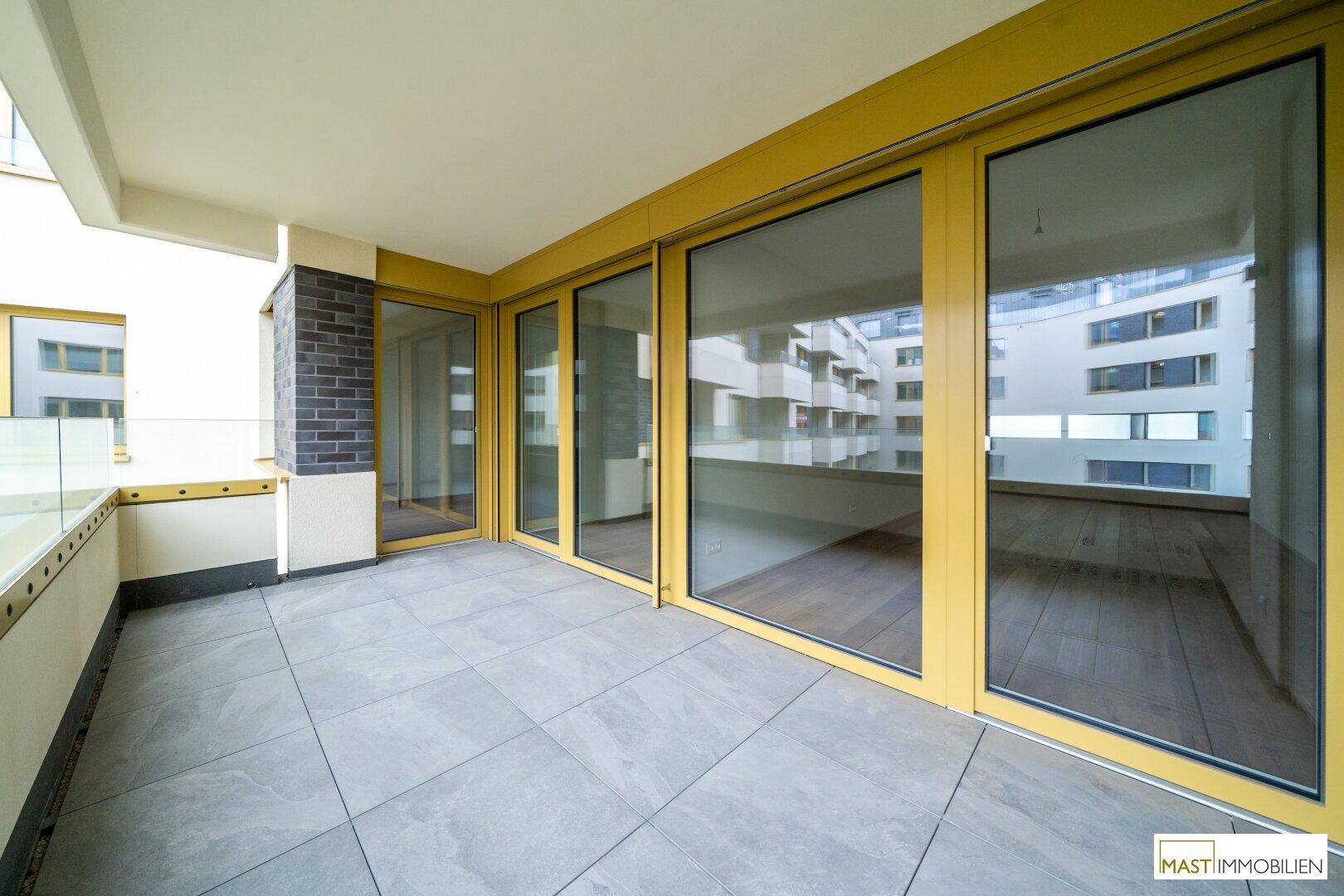 Heller Balkon mit Fliesenboden und großen Schiebetüren, die Zugang zum Innenbereich bieten.