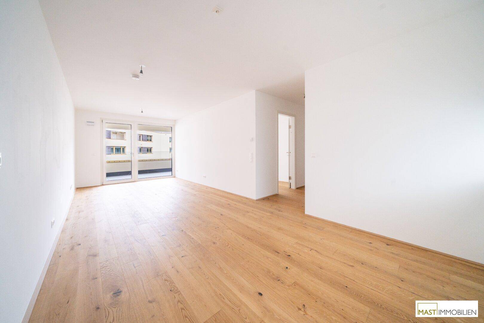 Heller, offener Raum mit Holzboden und Zugang zu einem Balkon, ideal für einen Wohnbereich.