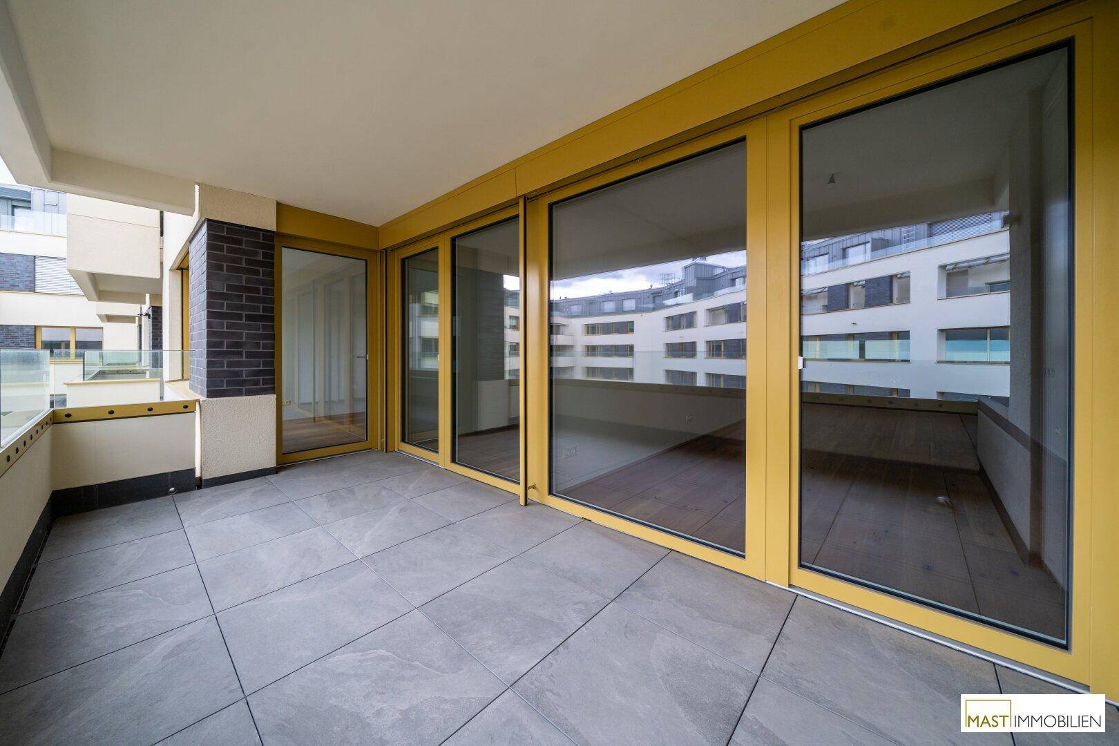 Heller Balkon mit Fliesenboden und großen Fenstern, die Zugang zum Innenbereich der Wohnung bieten.