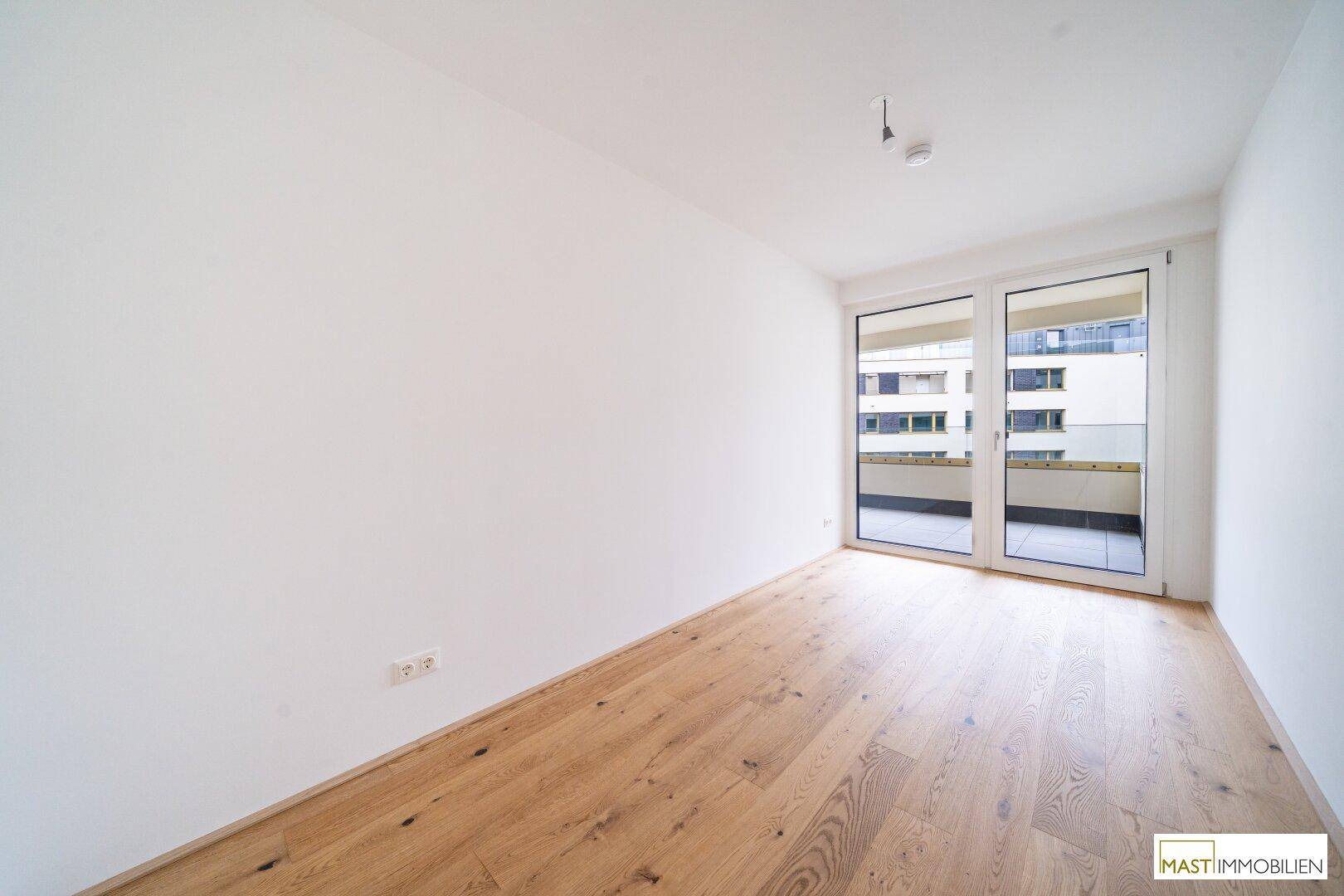 Helles Zimmer mit Parkettboden und großen Fenstern, die viel Tageslicht hereinlassen.