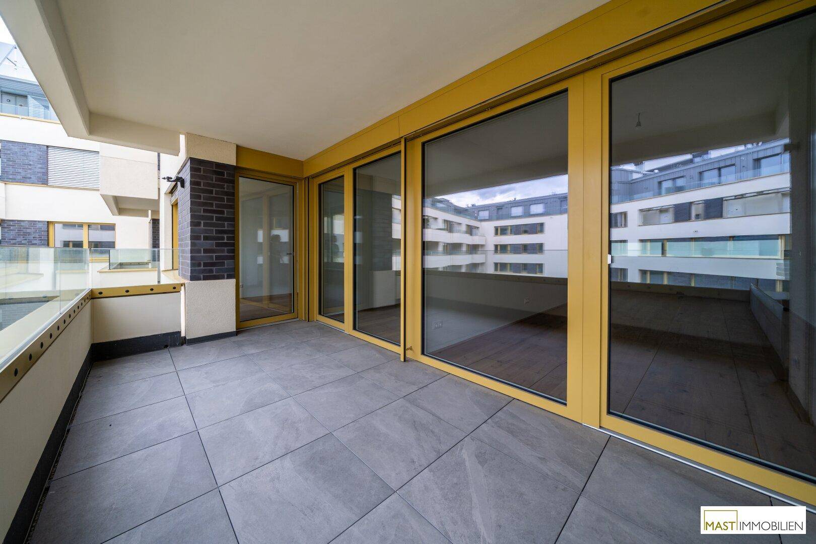 Breiter Balkon mit modernen Fliesen und großen Glasfronten, die viel Licht in die Innenräume lassen.