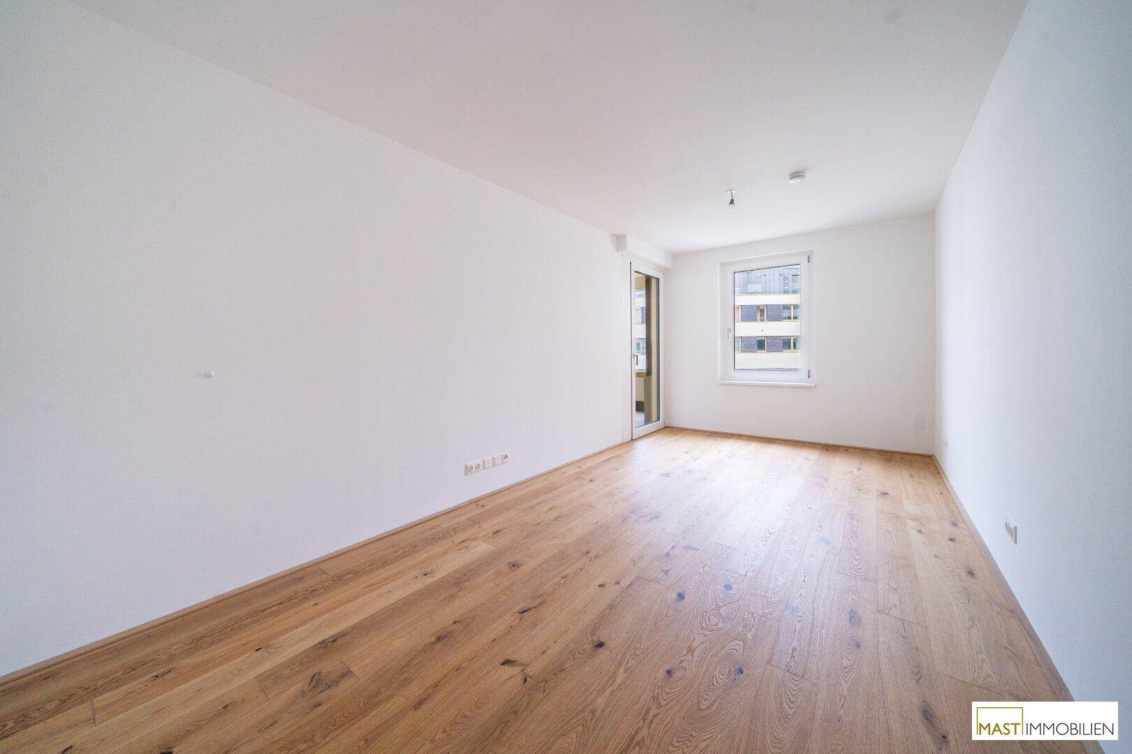 Leeres Zimmer mit hellem Parkettboden und einem Fenster, das den Raum angenehm erhellt.
