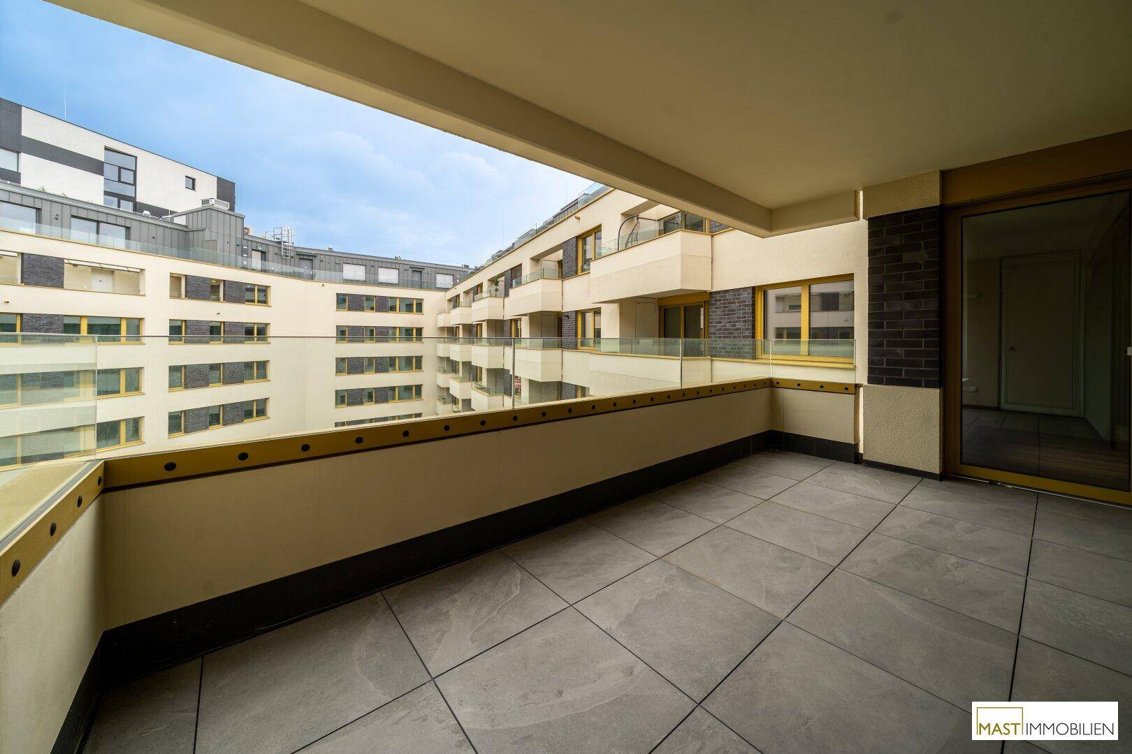 Großer Balkon mit Fliesenboden und Glasgeländer, umgeben von moderner Wohnarchitektur.