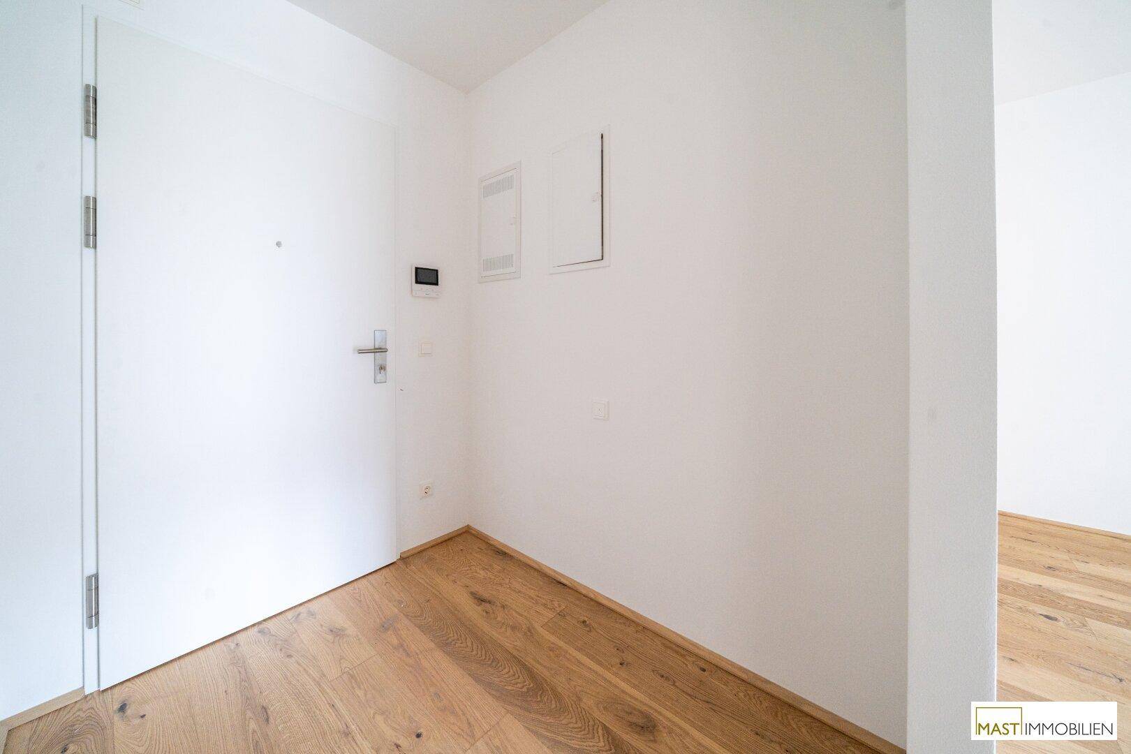 Eingangsbereich mit Holzboden und weißer Eingangstür, die zu den Wohnräumen führt.