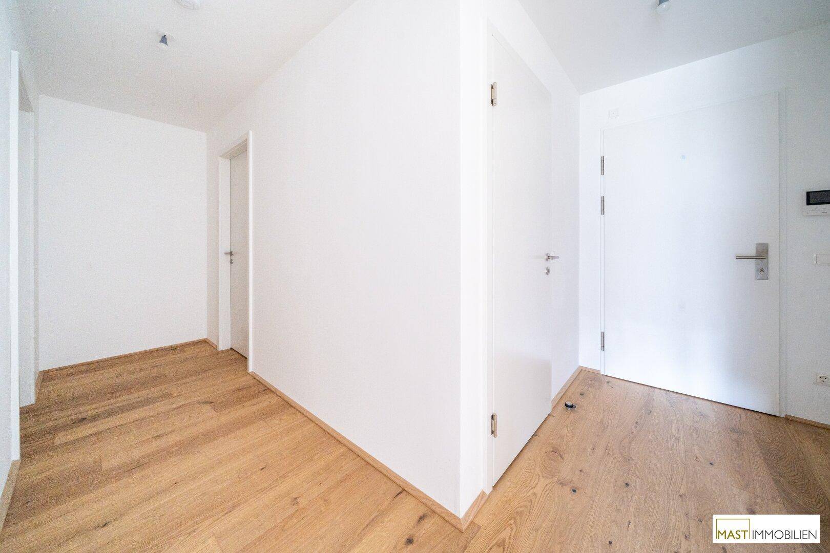 Heller Flur mit Holzboden und mehreren Türen, der verschiedene Räume miteinander verbindet.