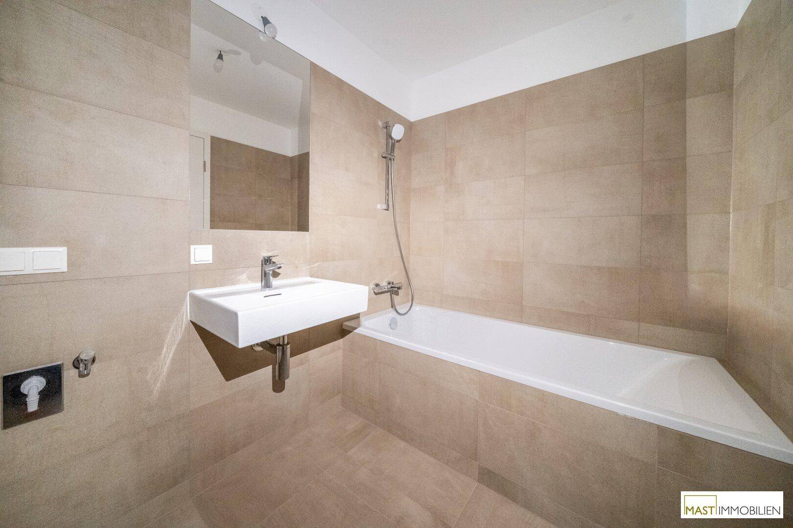 Modernes Badezimmer mit Badewanne, Waschbecken und beigefarbenen Fliesen an Wänden und Boden.
