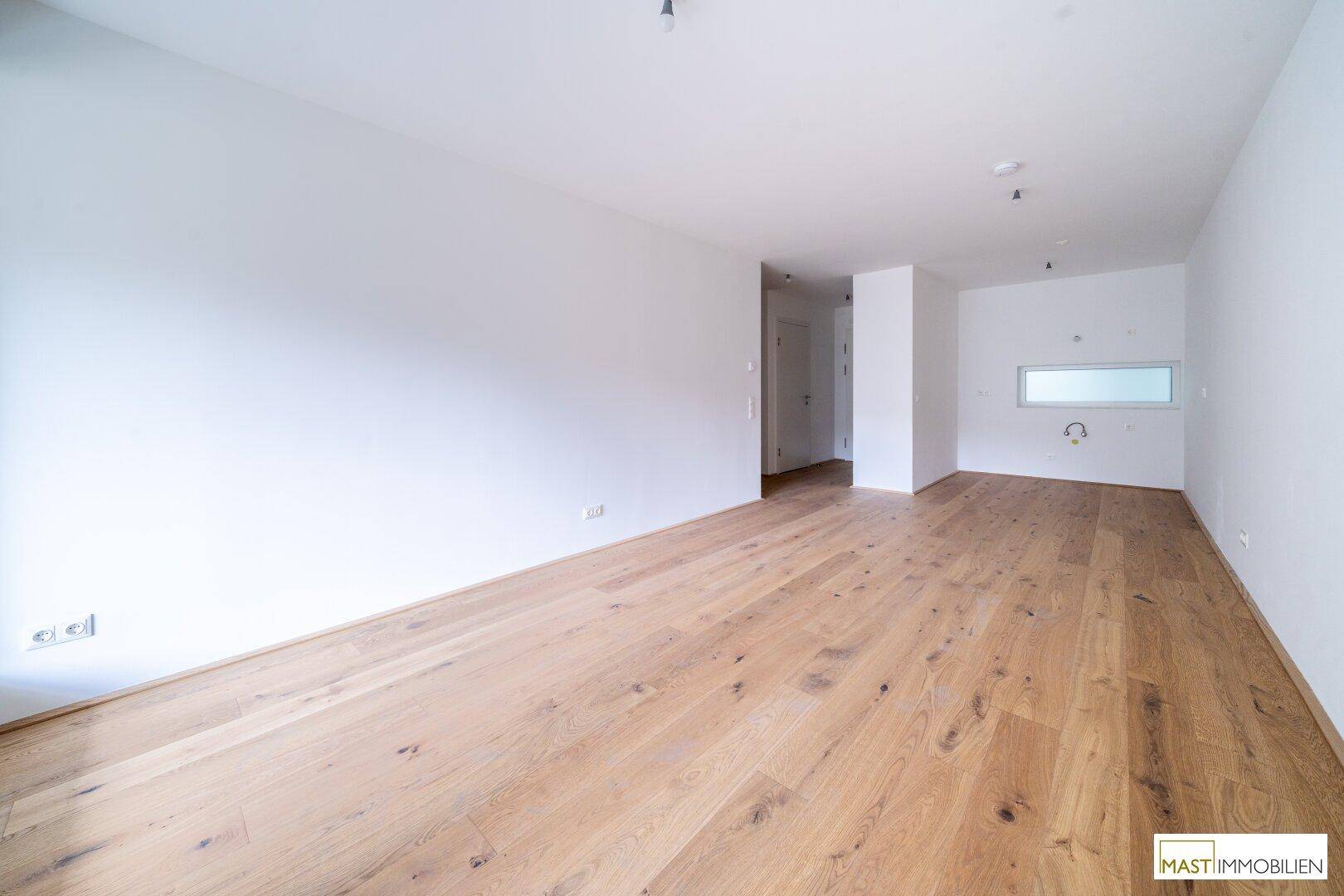 Geräumiger Raum mit Parkettboden und Anschlüssen für eine Küche, bereit für die Installation.