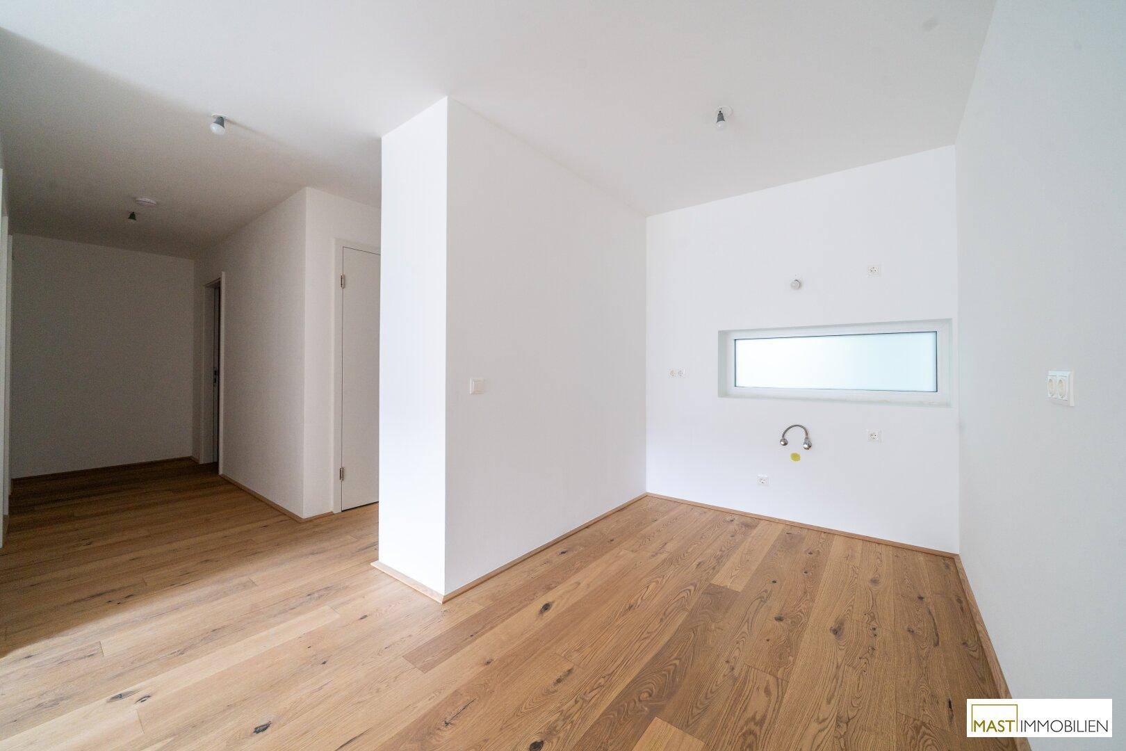 Heller Küchenbereich mit Parkettboden und Fenster, vorbereitet für die Kücheneinrichtung.