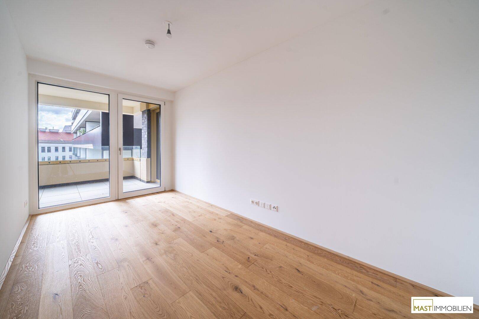 Lichtdurchflutetes Schlafzimmer mit Parkettboden und direktem Zugang zum Balkon.