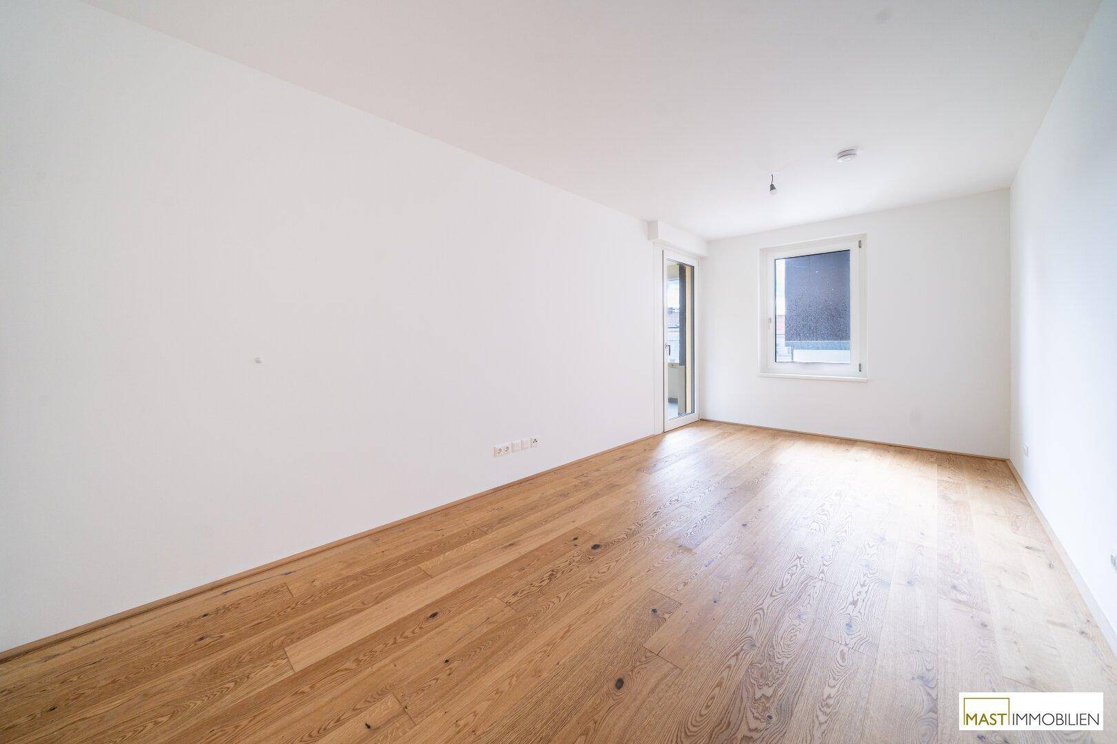 Helles Zimmer mit Parkettboden und einem Fenster, ideal als Schlaf- oder Arbeitszimmer.