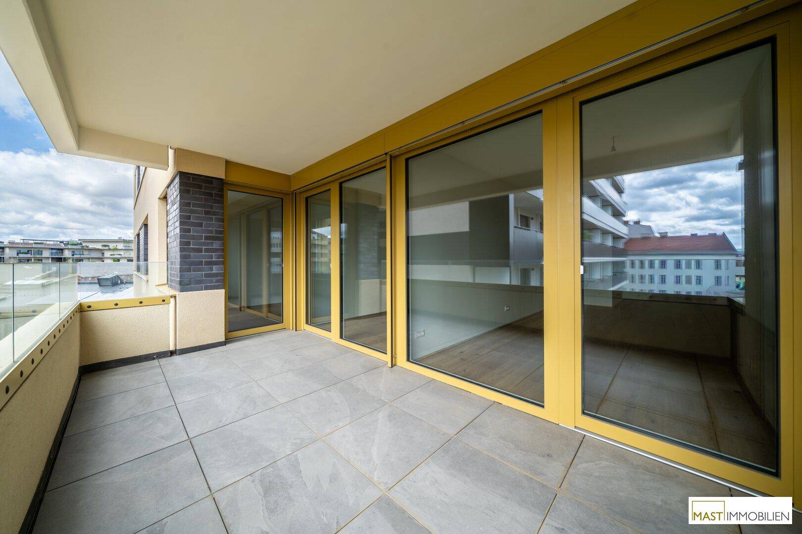 Großer Balkon mit Fliesenboden und breiten Glasfronten, die viel Licht in die Innenräume lassen.
