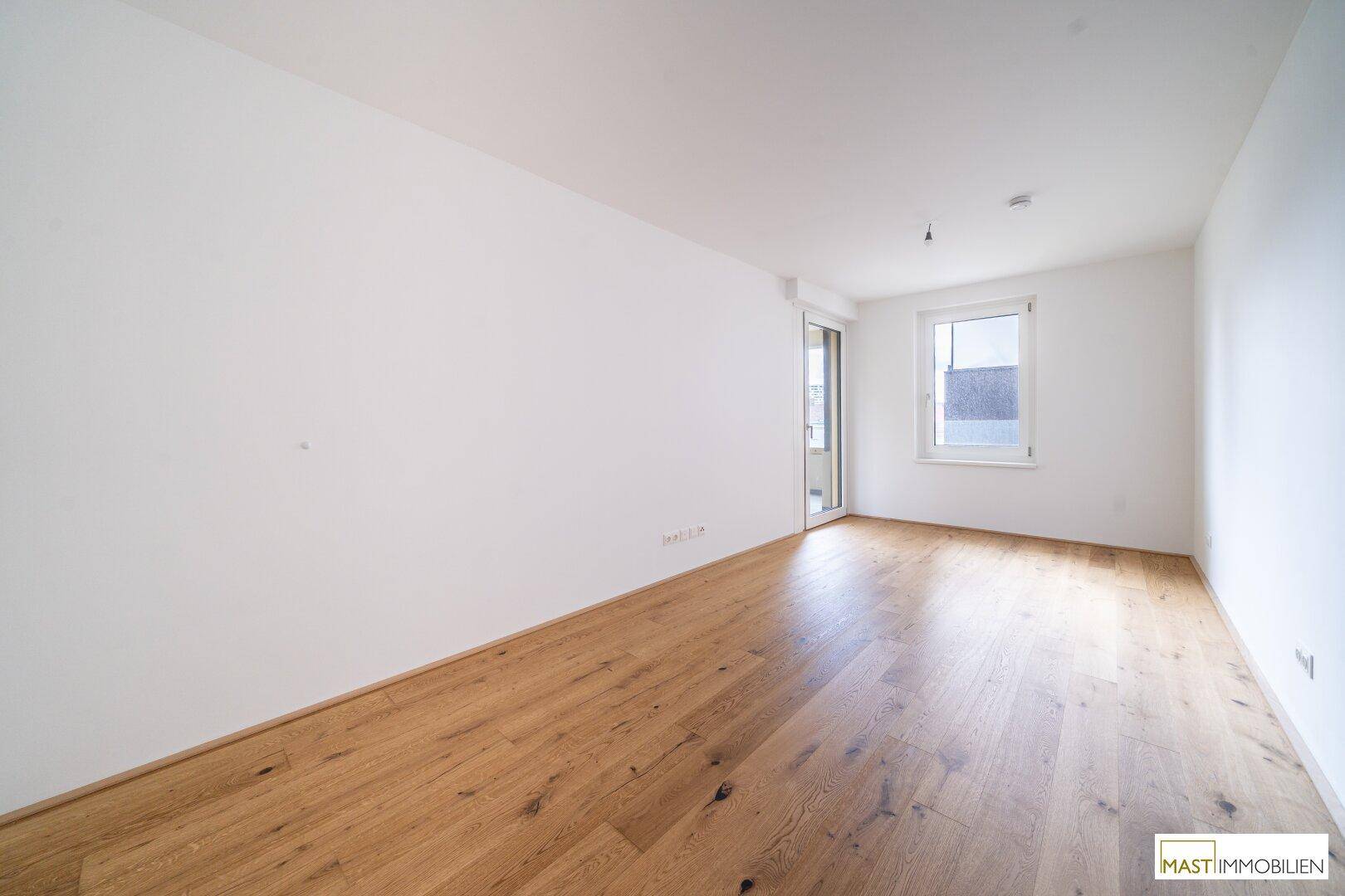 Unmöbliertes Zimmer mit Holzboden, großem Fenster und Zugang zu einem weiteren Balkon.