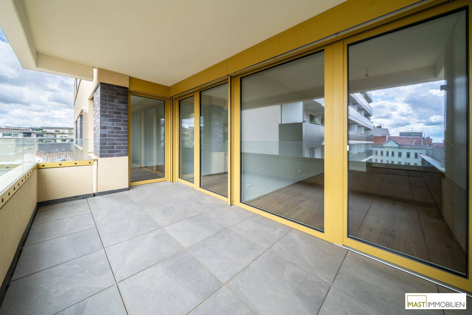Großer Balkon mit Schiebetüren und Fliesenboden, bietet viel Licht und einen schönen Ausblick.
