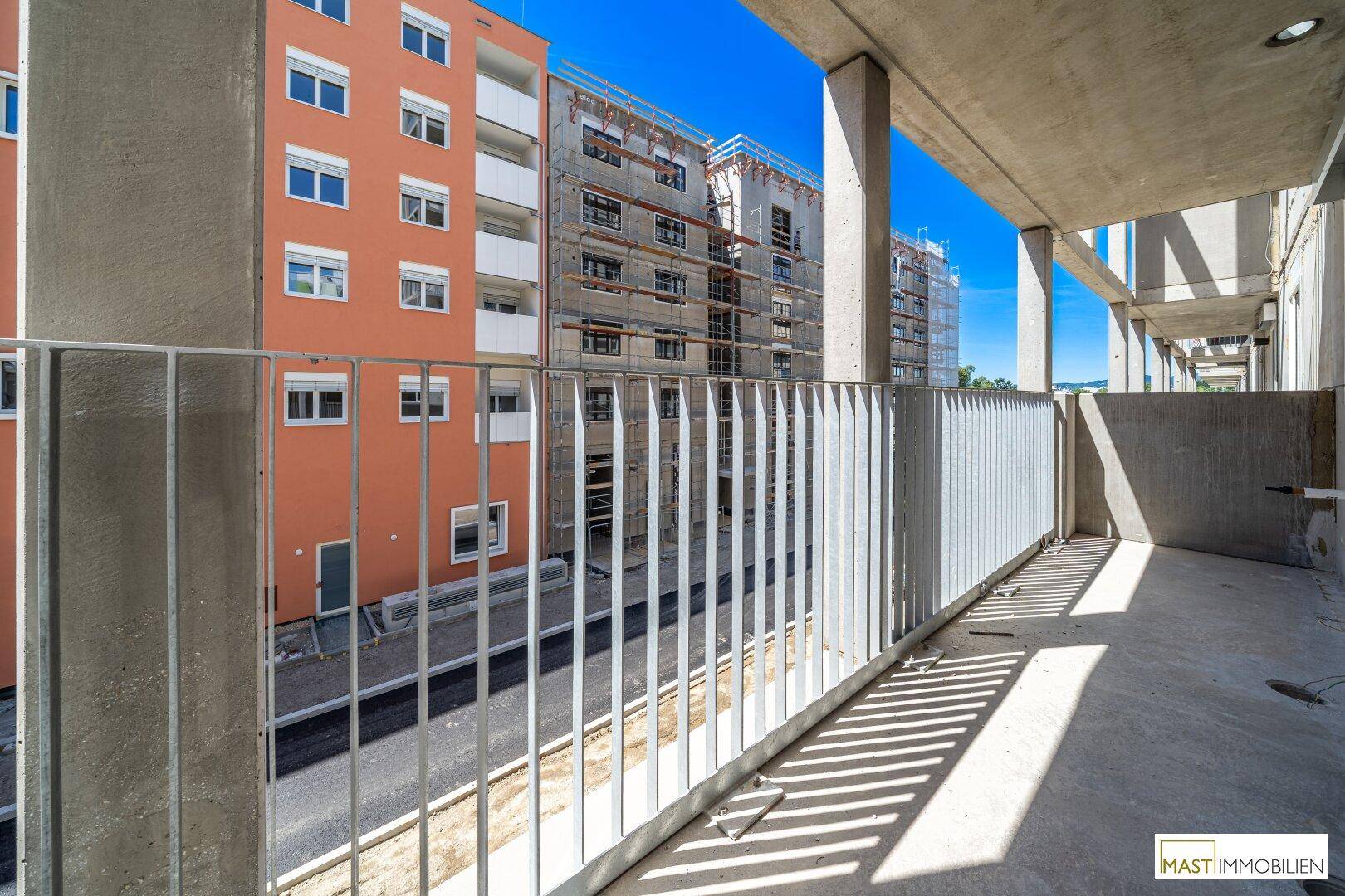 Balkon eines Neubaus mit Metallgeländer und Aussicht auf die städtische Umgebung und weitere Bauprojekte.