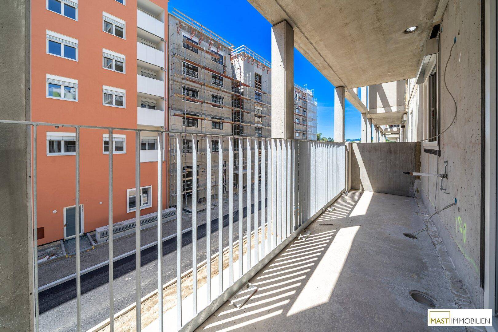 Unmöblierter Balkon mit Betonboden und Blick auf die umliegenden Gebäude und den blauen Himmel.