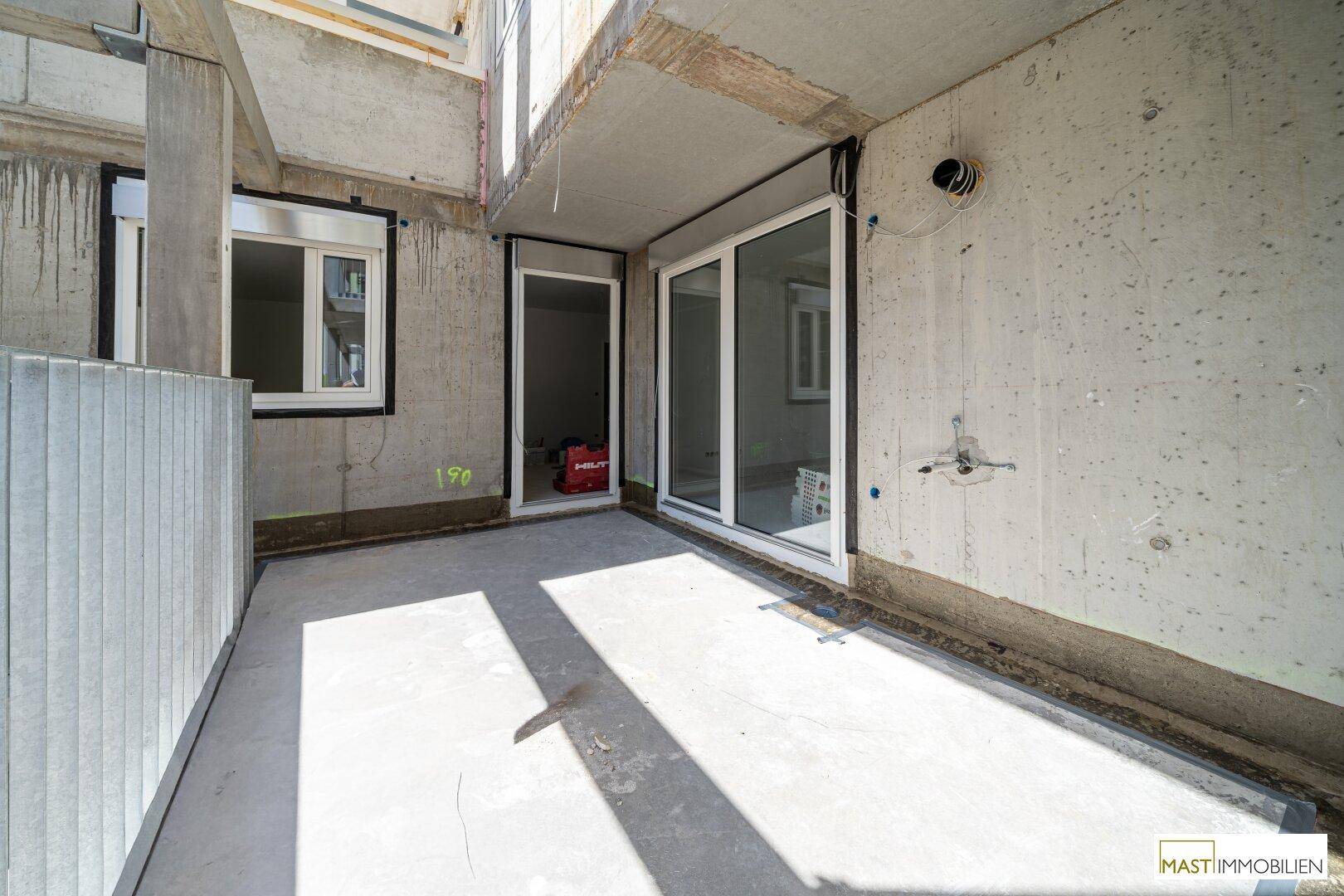 Balkon im Rohzustand mit Zugangstüren und Fenster zu den zukünftigen Wohnräumen.