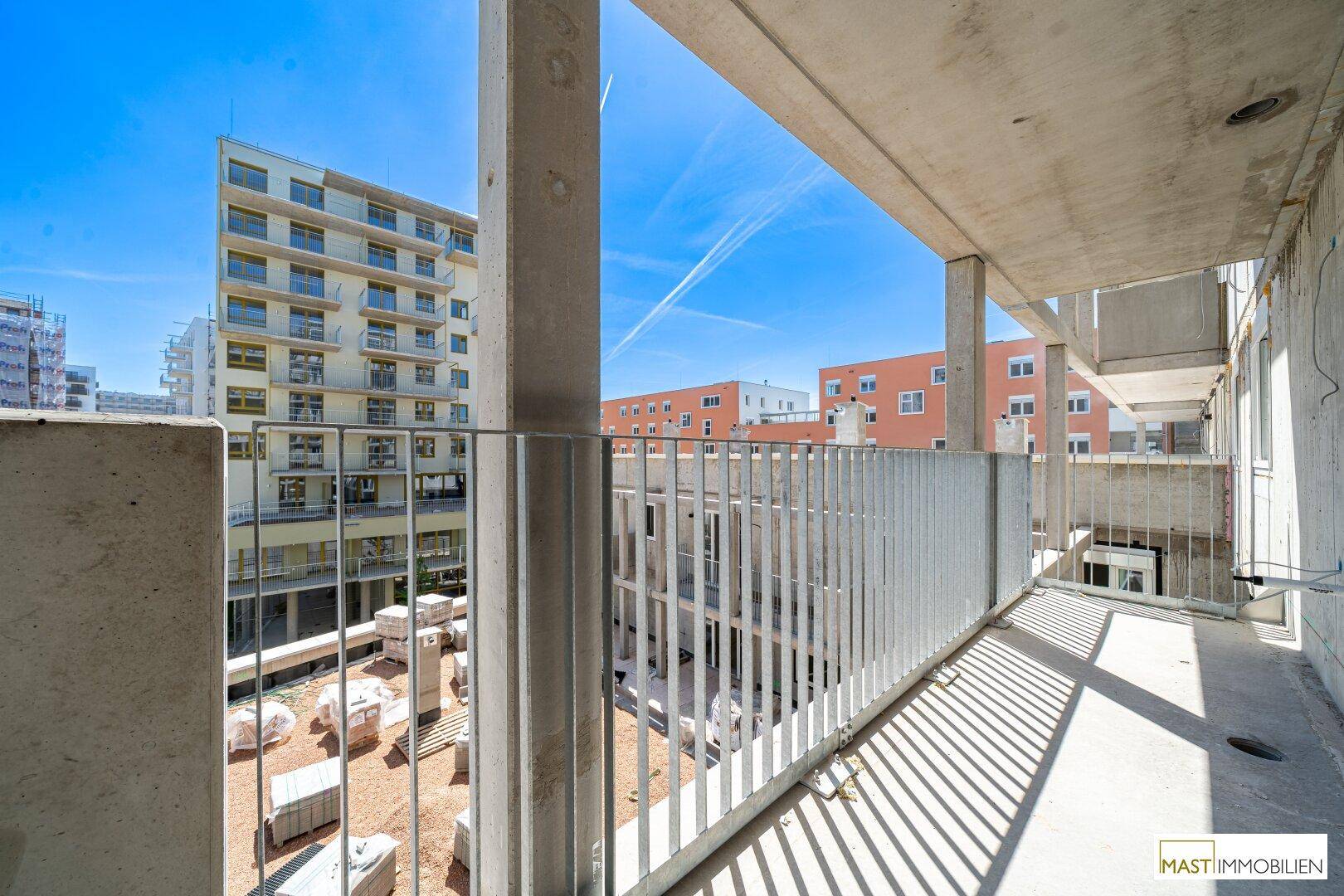 Sonniger Balkon mit weitem Blick über die Baustelle und die modernen Wohngebäude.