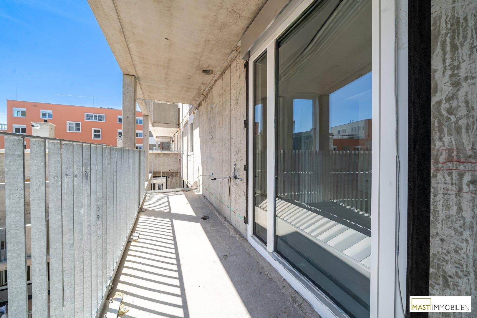 Langer Balkon mit Schiebetürzugang zum Innenbereich und Blick auf weitere Gebäude.