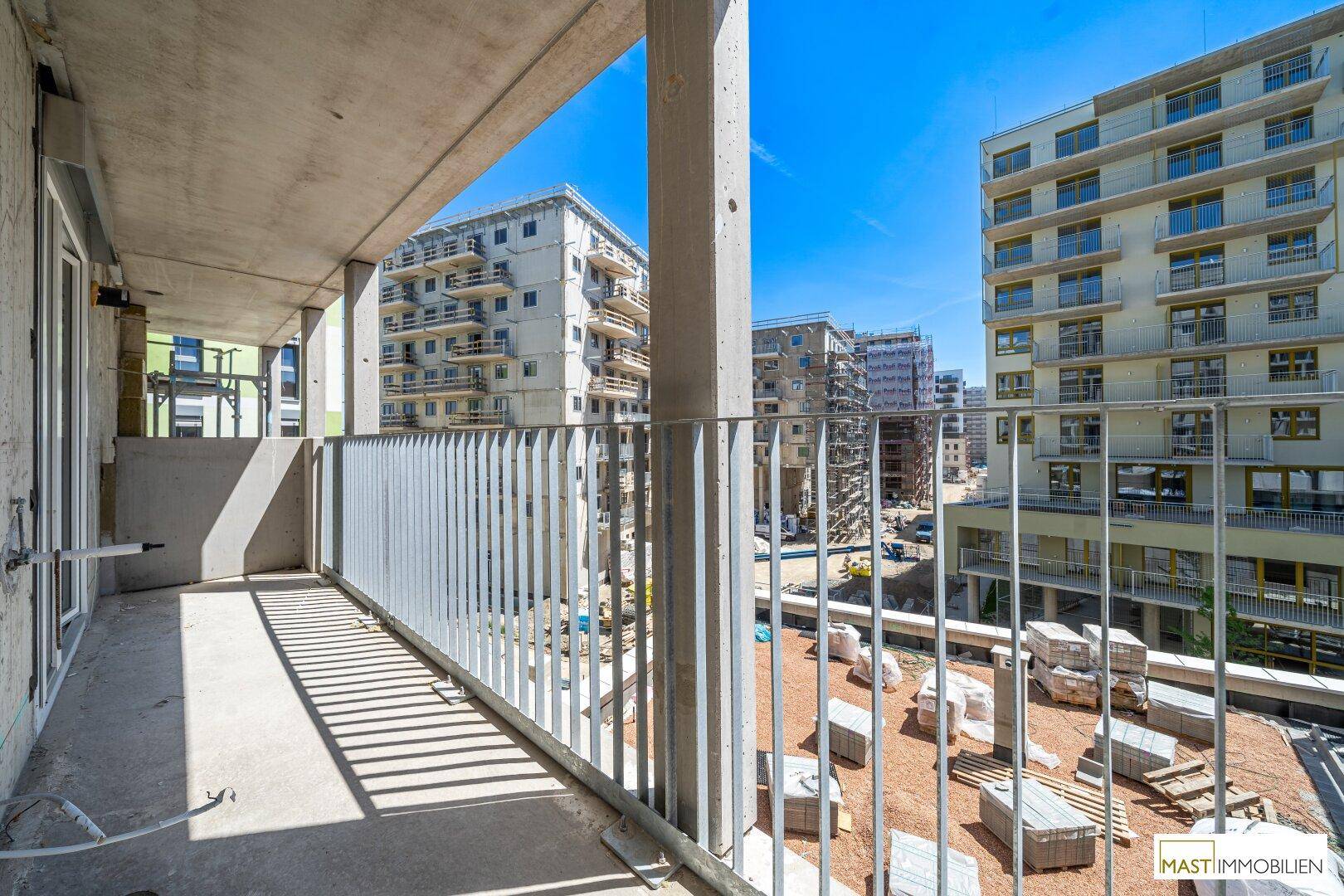 Geräumiger Balkon mit Blick auf die umliegenden Neubauten und die Baustelle bei sonnigem Wetter.