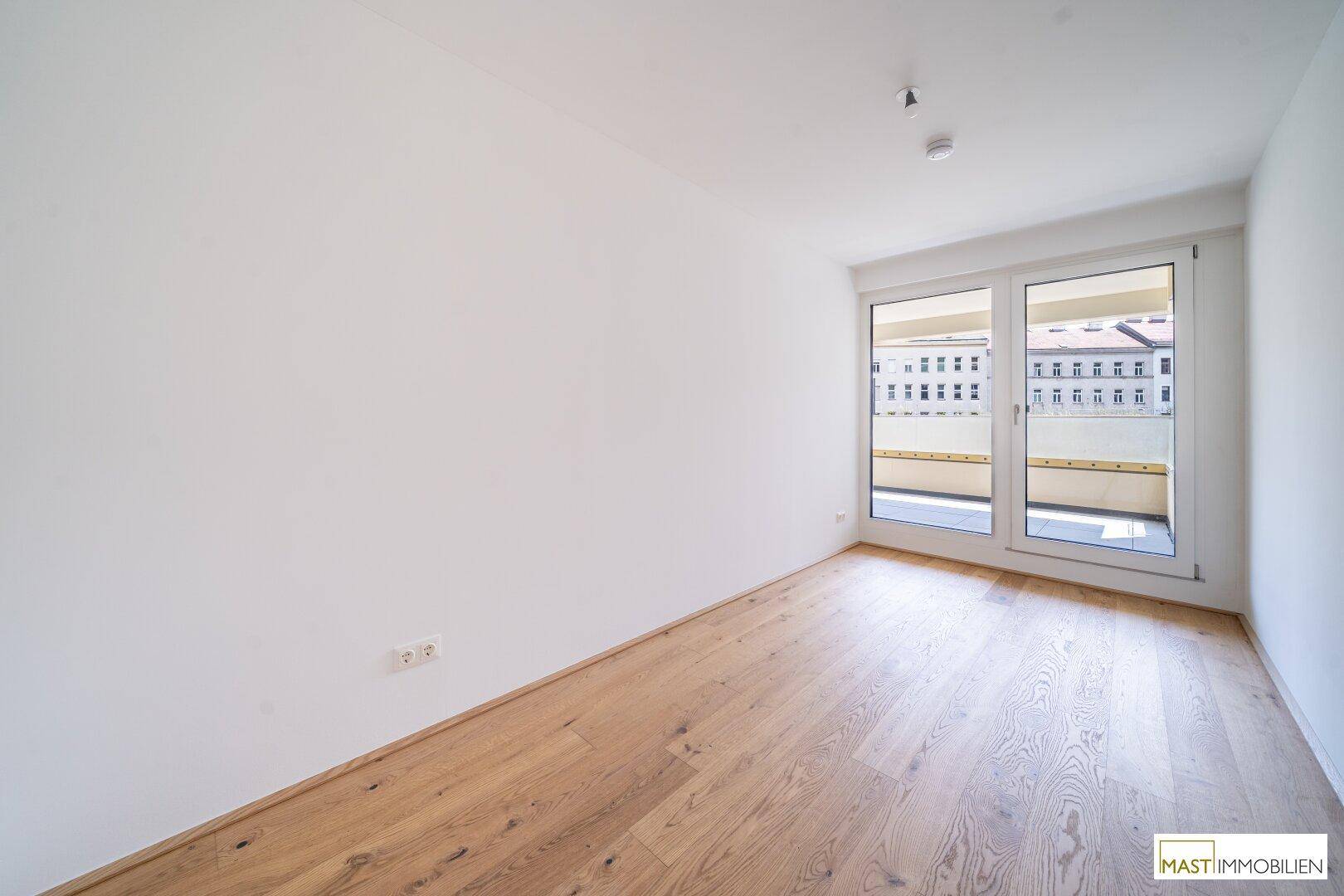 Helles Schlafzimmer mit Parkettboden und breiter Schiebetür zum Balkon.