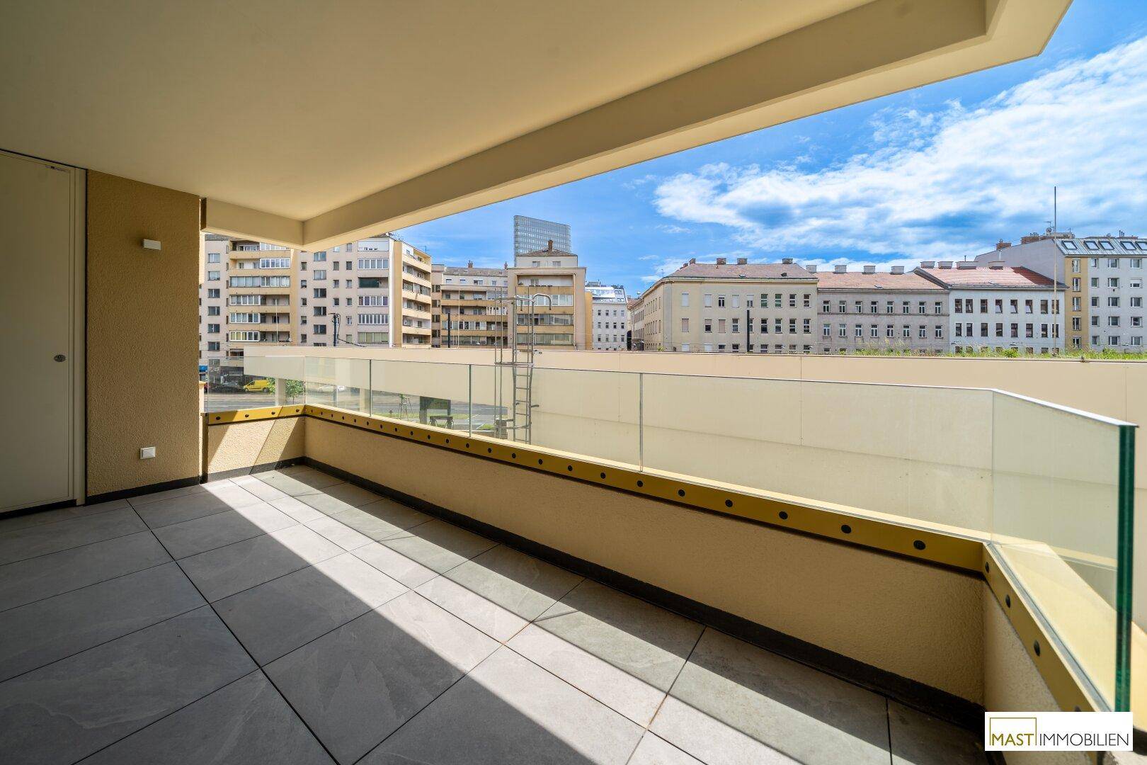 Großer Balkon mit Glasgeländer und Blick auf die umliegenden Gebäude der Stadt.
