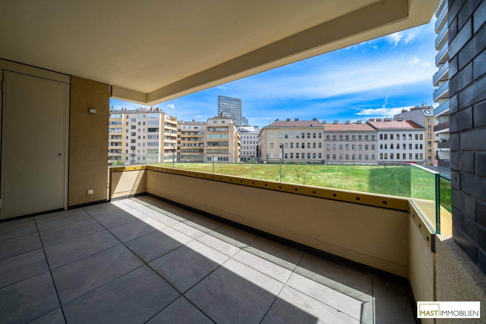 Geräumiger Balkon mit Fliesenboden und Glasgeländer, bietet einen weiten Blick über Grünflächen und die Stadt.