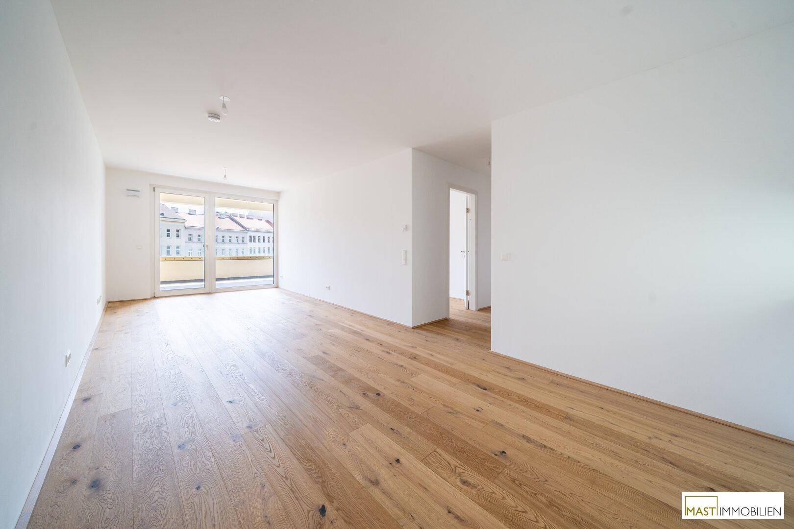 Großzügiger Wohnbereich mit Eichenparkett und Zugang zu einem Balkon, ideal für helle Einrichtung.