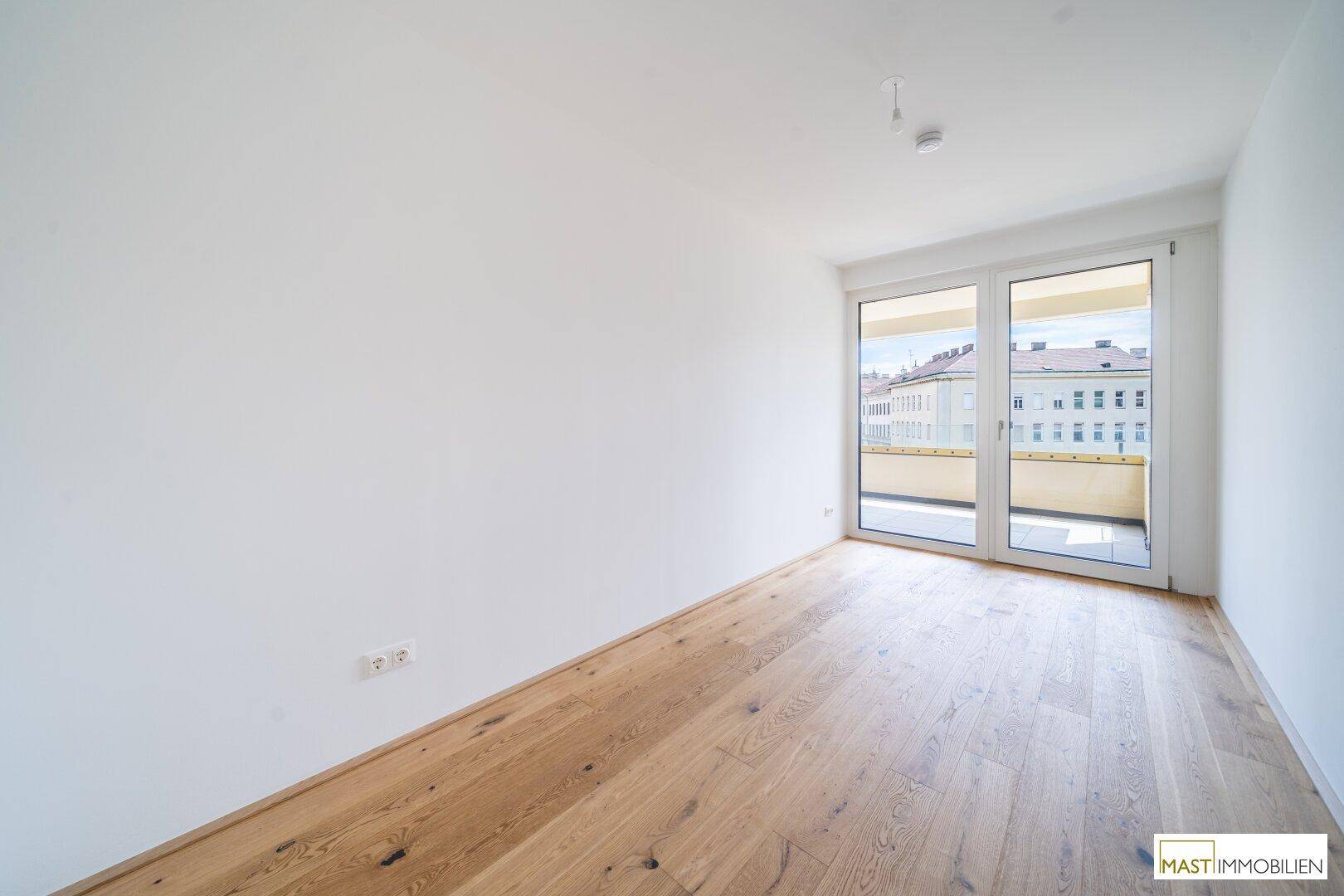 Helles Schlafzimmer mit Holzboden und großer Glastür, die viel Tageslicht hereinlässt.