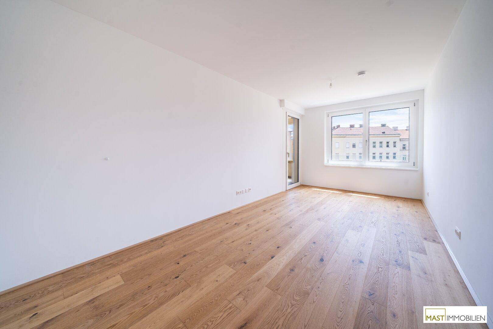 Freundliches Zimmer mit Parkettboden und einem großen Fenster, das eine angenehme Atmosphäre schafft.