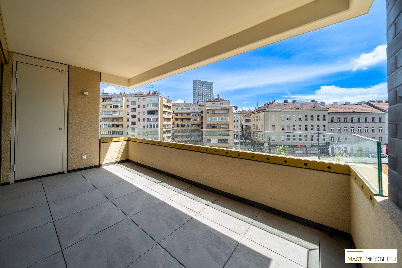 Sonniger Balkon mit Fliesenboden und Blick auf die umliegende Stadtarchitektur unter blauem Himmel.
