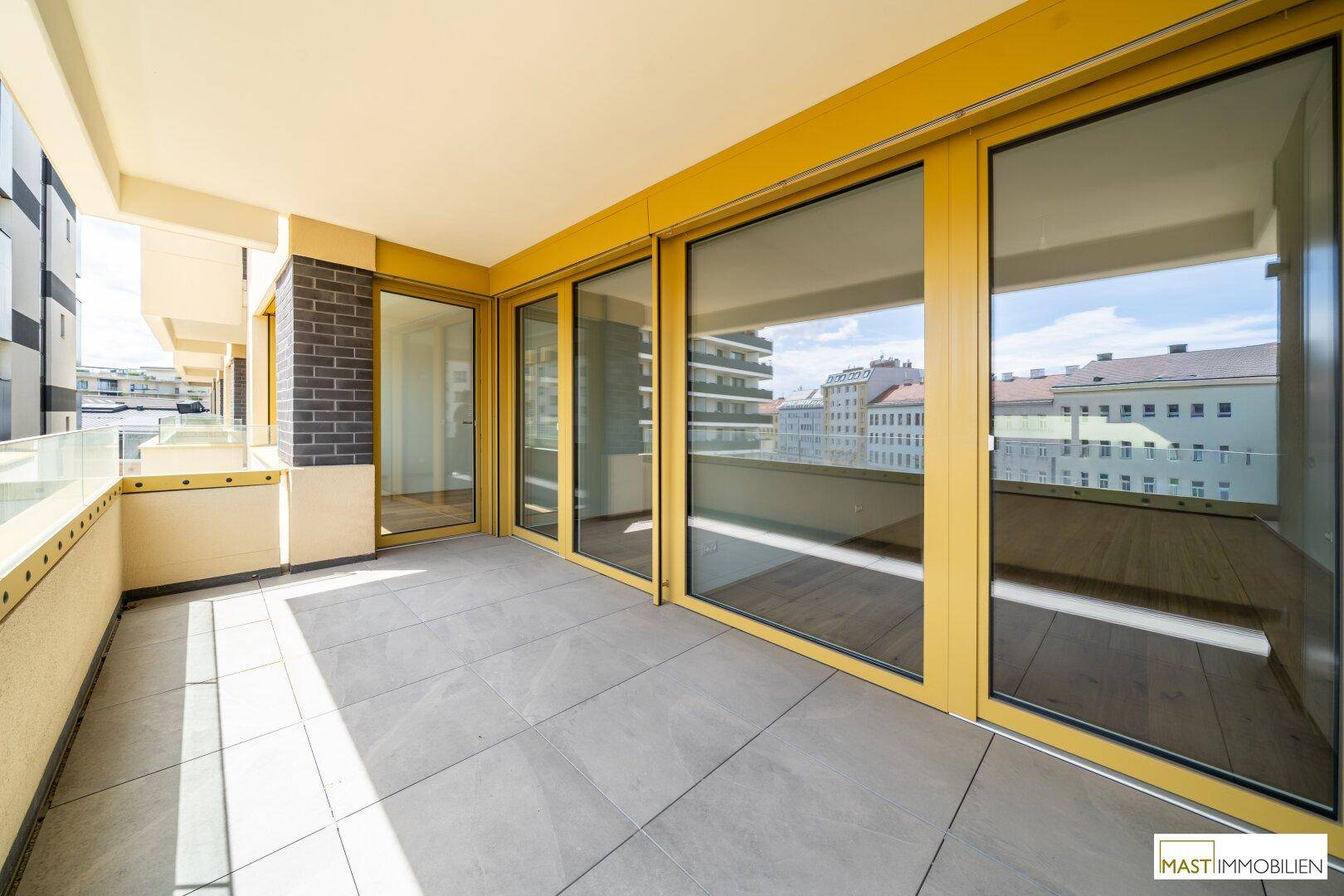 Moderner Balkon mit großen Glasfronten und Fliesenboden, der viel Licht in die Innenräume lässt.