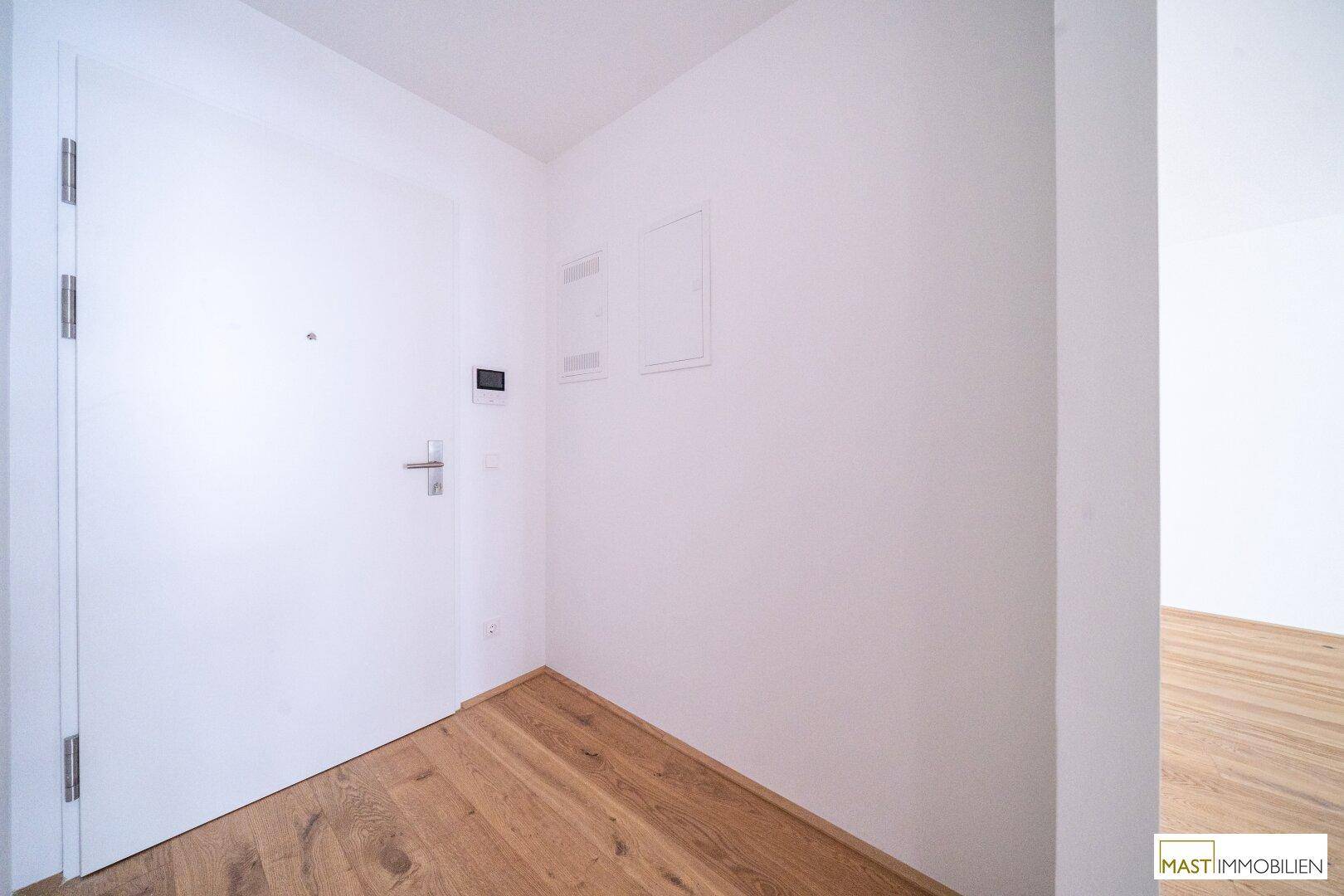 Heller Eingangsbereich mit Holzboden und weißer Tür, modern und einladend gestaltet.