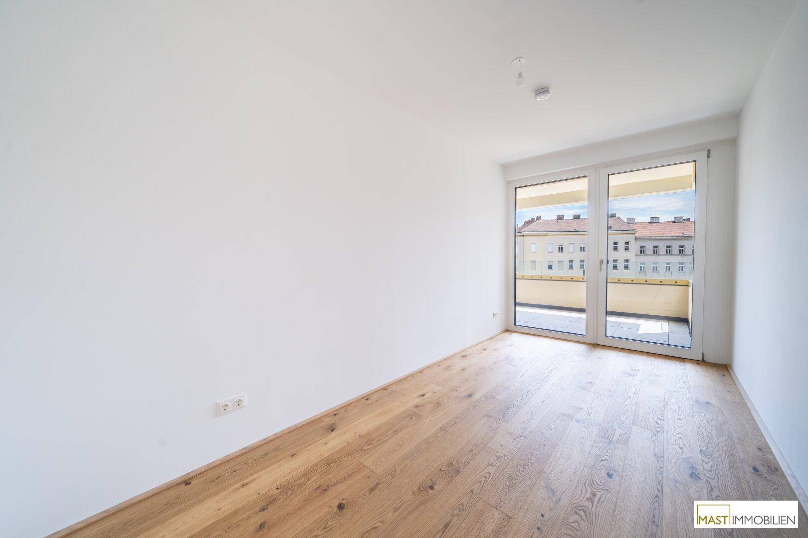 Leeres Schlafzimmer mit Holzboden und Zugang zu einem Balkon, hell und modern.