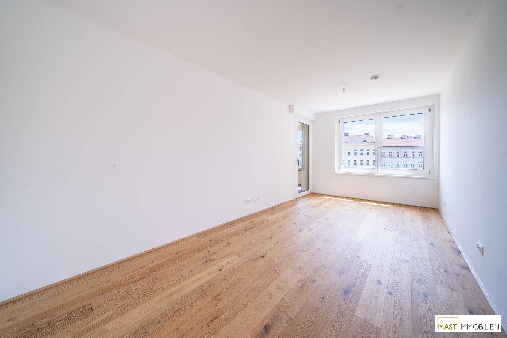 Helles, leeres Zimmer mit Holzboden und großem Fenster, ideal als Schlaf- oder Arbeitszimmer.