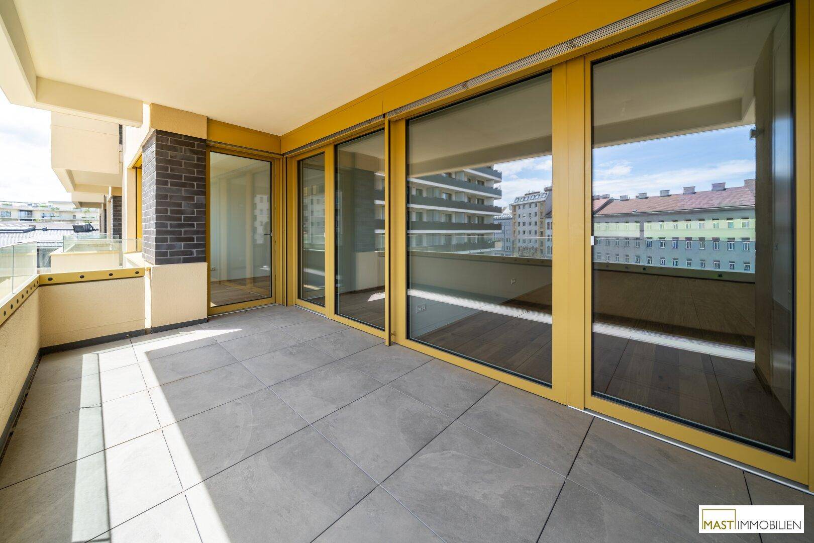 Geräumige Terrasse mit großen Glasfronten und Fliesenboden, bietet viel Platz im Freien.