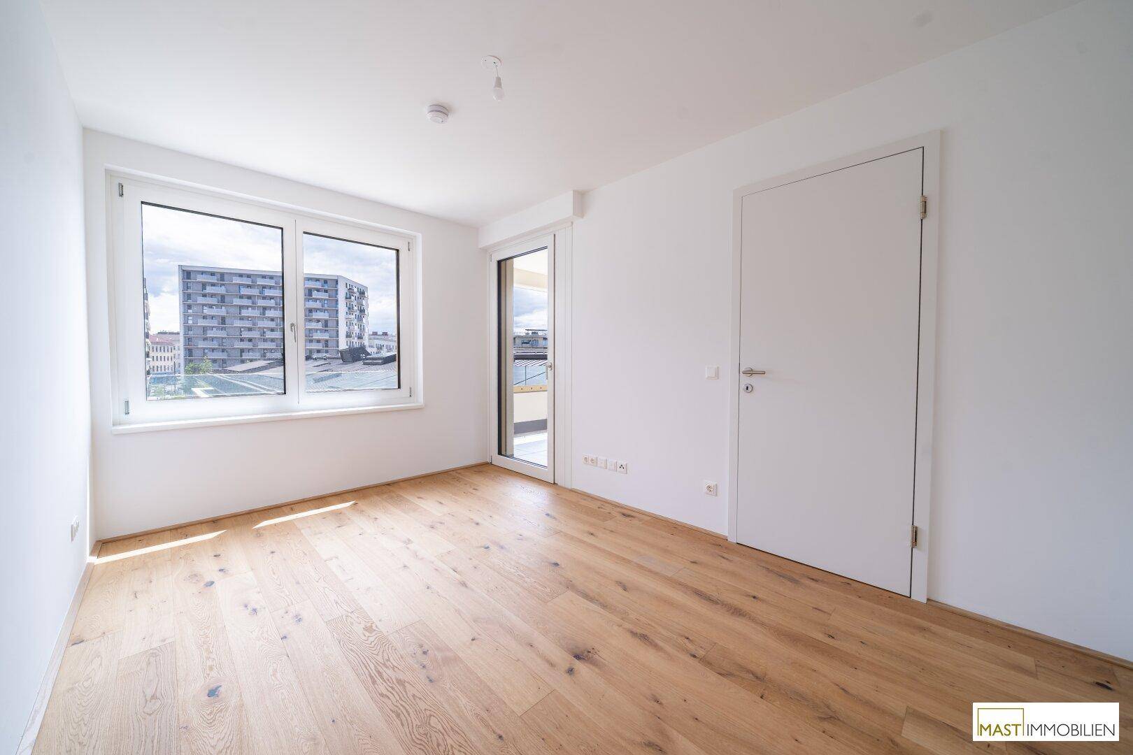 Helles Schlafzimmer mit Parkettboden, großen Fenstern und Zugang zu einem Außenbereich.