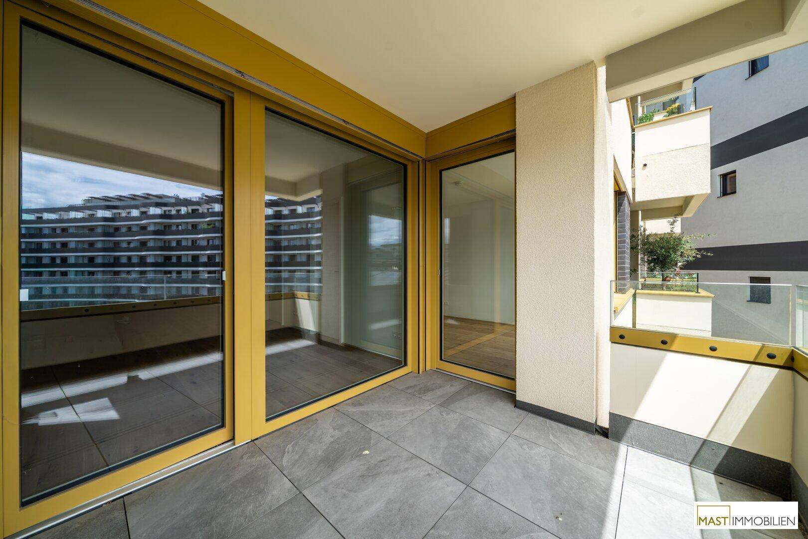 Heller Balkon mit Fliesenboden und großen Glasschiebetüren, die viel Licht in den Innenraum lassen.